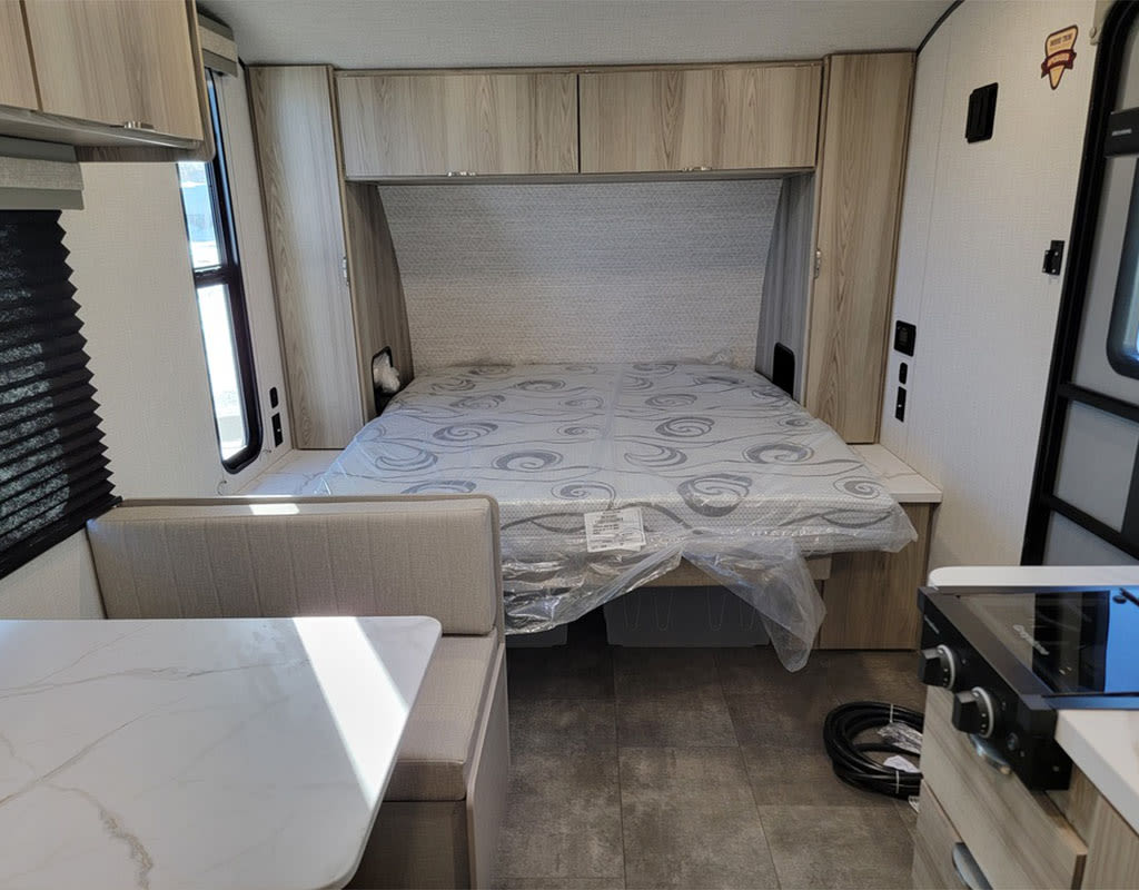 This rv rental offers a modern interior with a central bed, dinette, and partial kitchen. Features light wood cabinets and grey accents.. Forest River Salem 2025