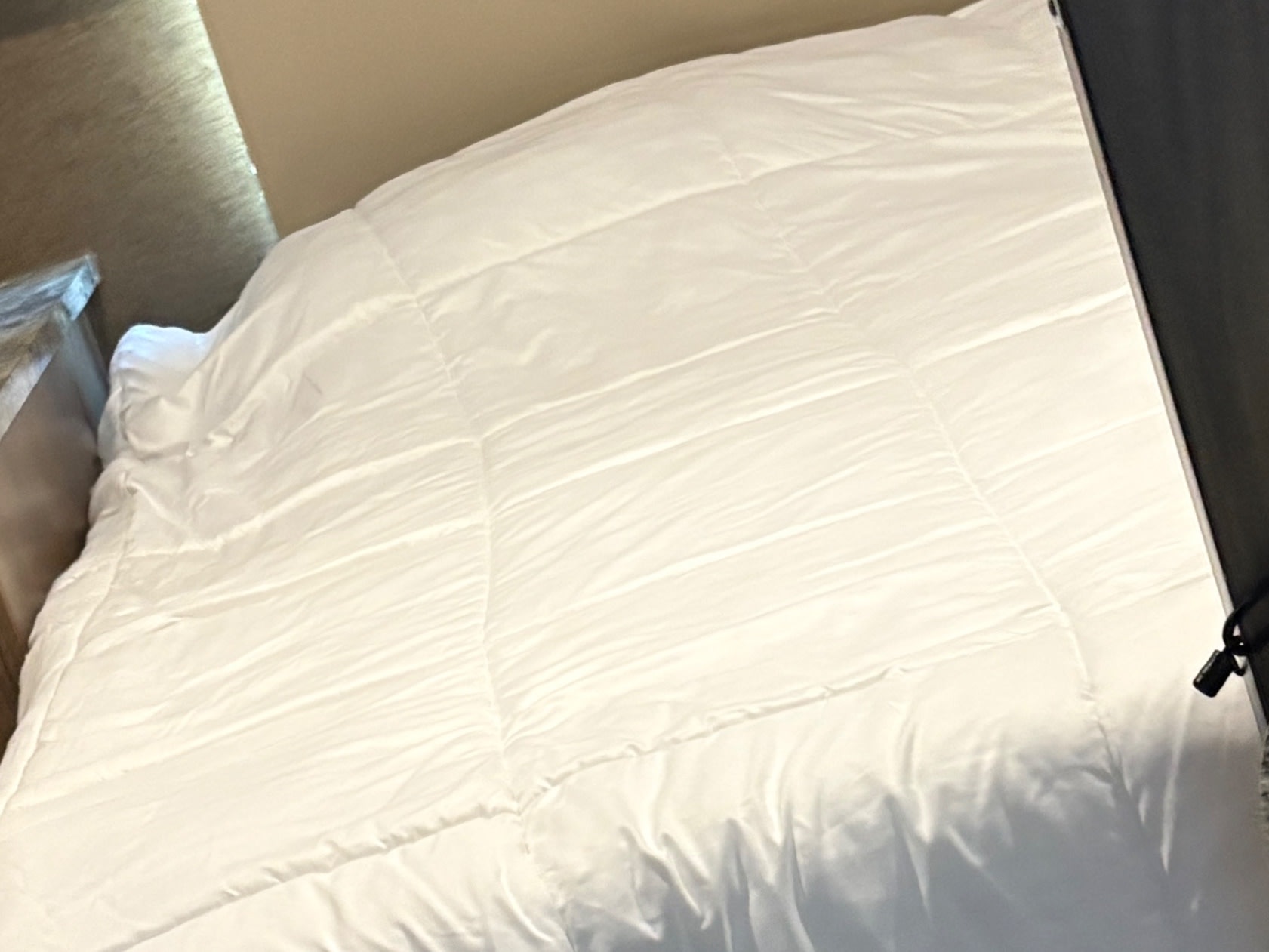 A neatly made bed with a white quilted comforter inside an RV rental. Provides a comfortable sleeping area with a bedside surface.. Forest River Coachmen Prism 2018