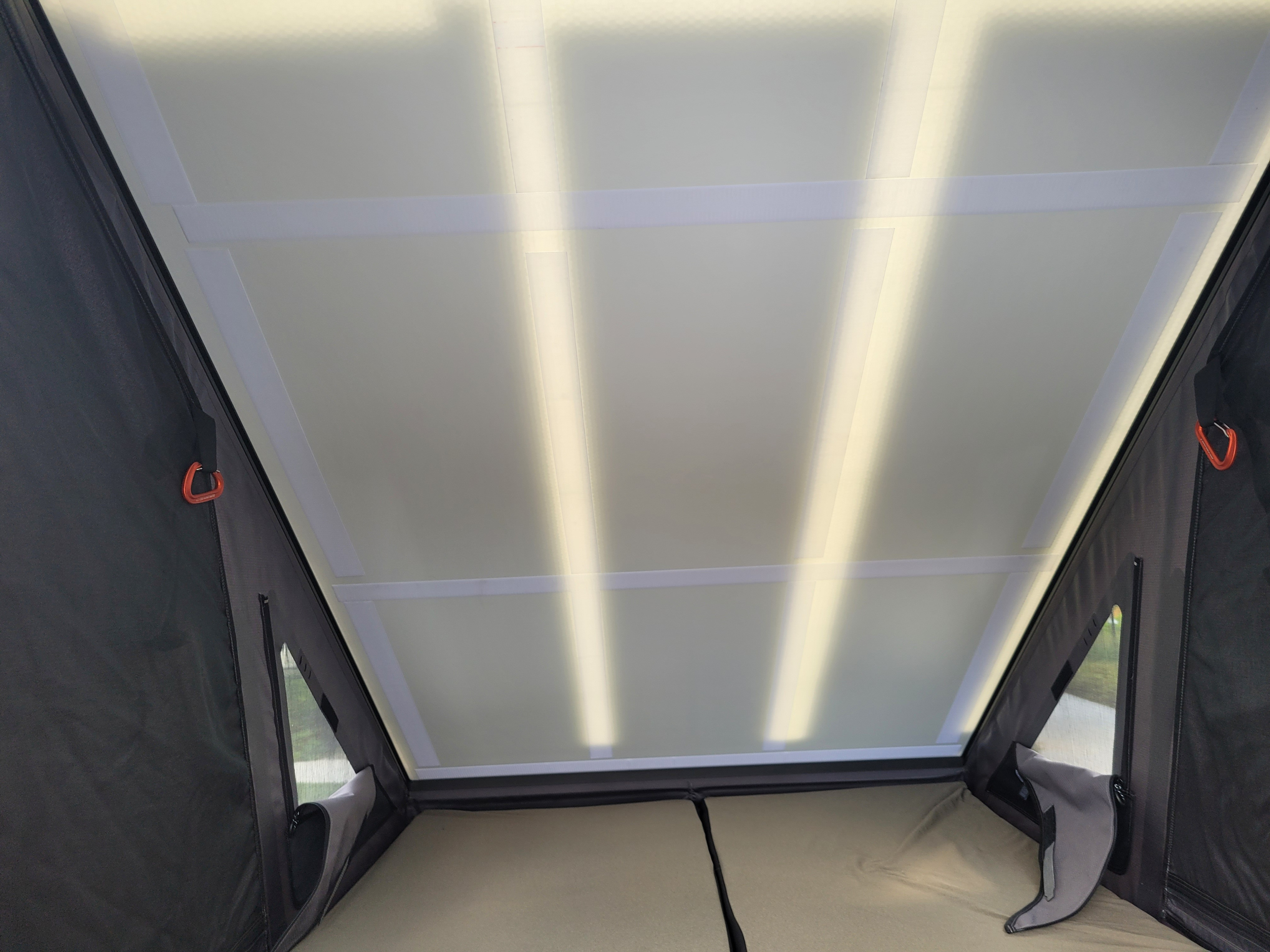 RV rental rooftop tent interior: Sleeping area with light-filtering ceiling, side mesh window, and red carabiner visible.. Rivian R1T 2023