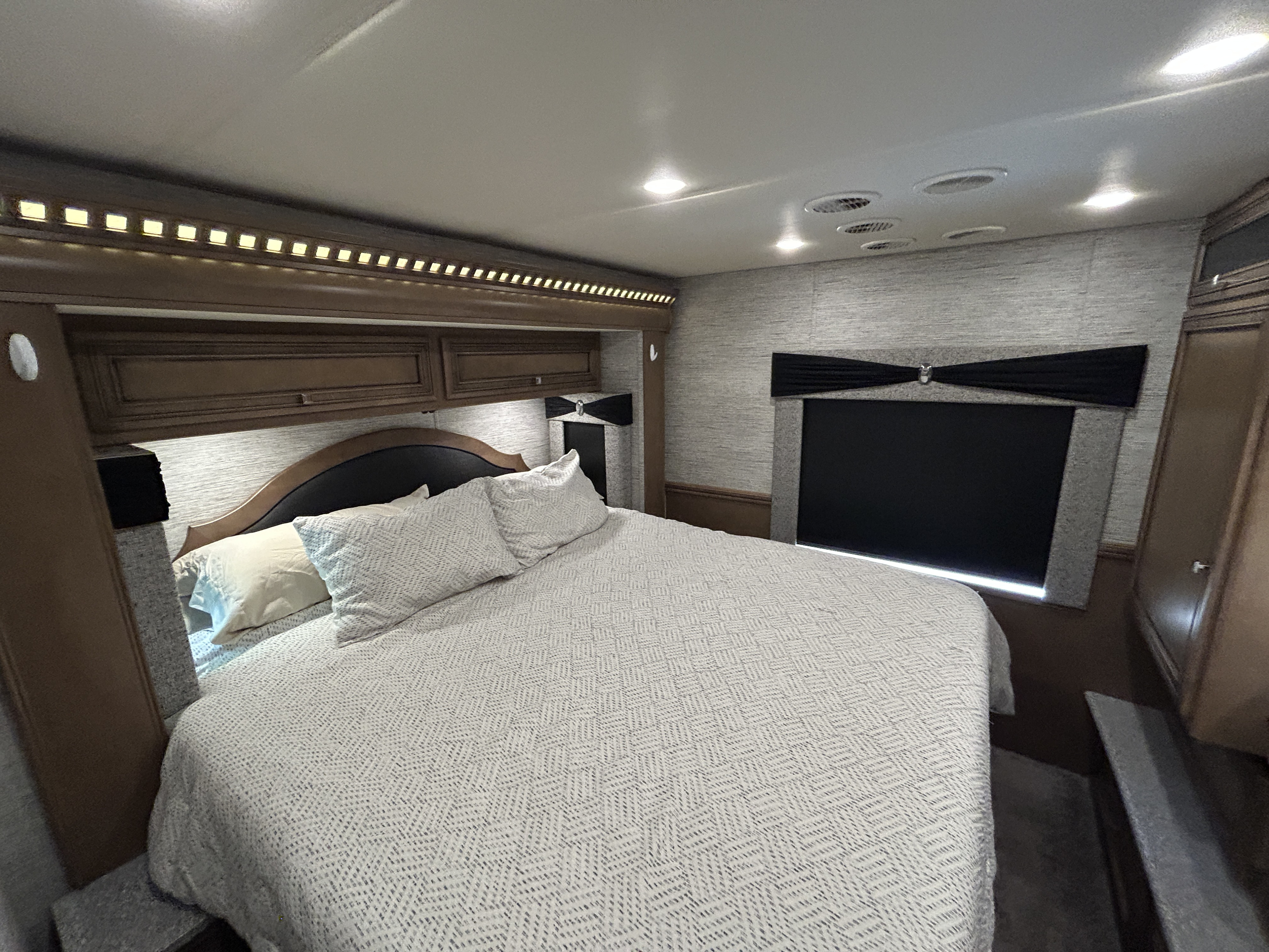 This inviting RV rental bedroom features a spacious bed with patterned bedding, overhead storage, and soft, recessed lighting.. Newmar Bay Star 2019