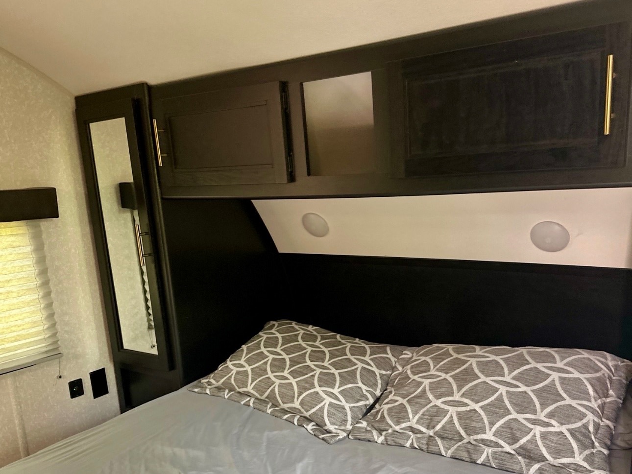 Cozy RV rental bedroom: dark overhead cabinets, mirrored wardrobe, and patterned pillows on a grey bed, offering storage and comfort.. Forest River Cherokee 2022