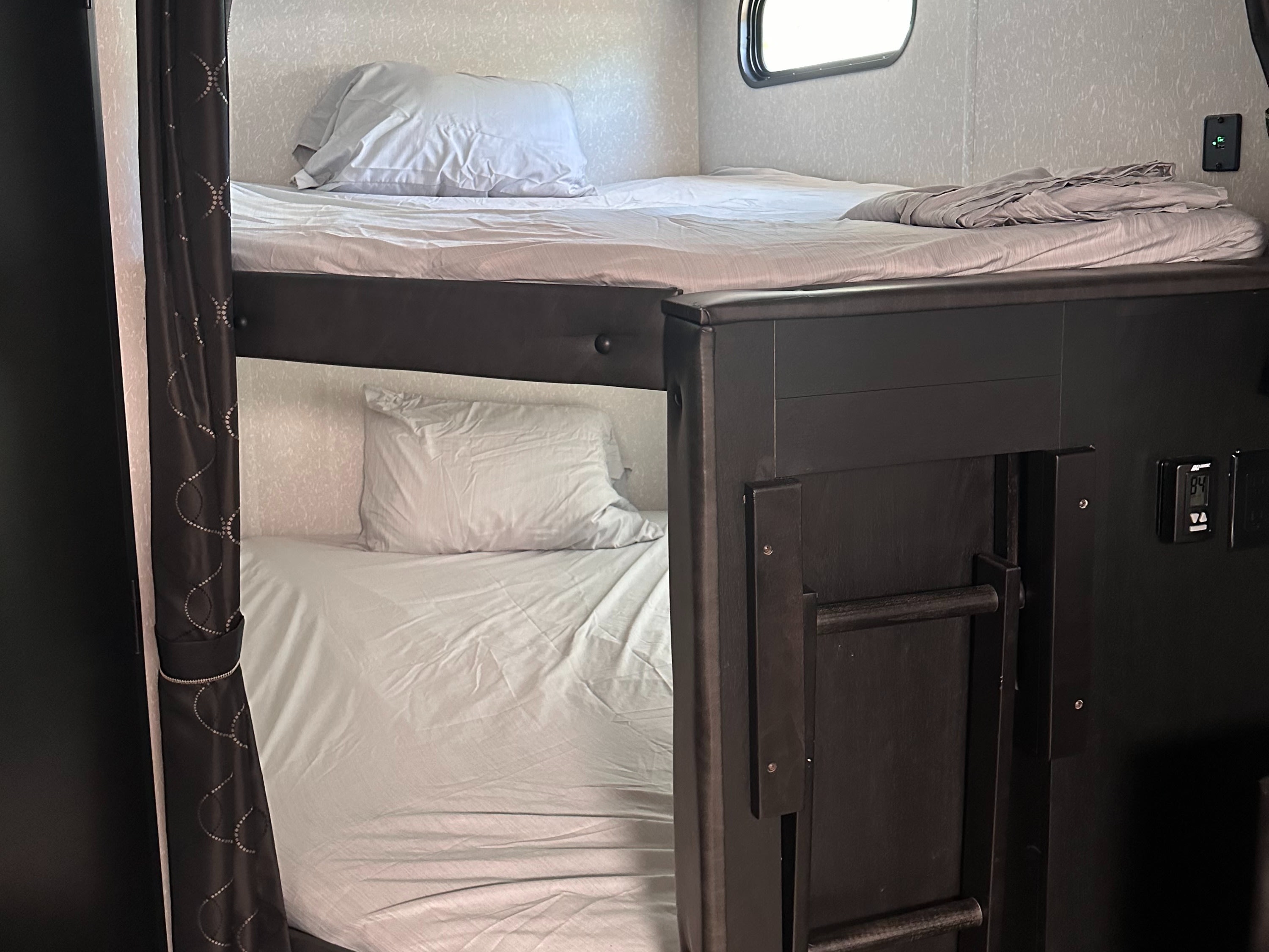 RV rental interior featuring a set of dark bunk beds with fresh white linens, a window, and dark privacy curtains.. Forest River Cherokee 2022