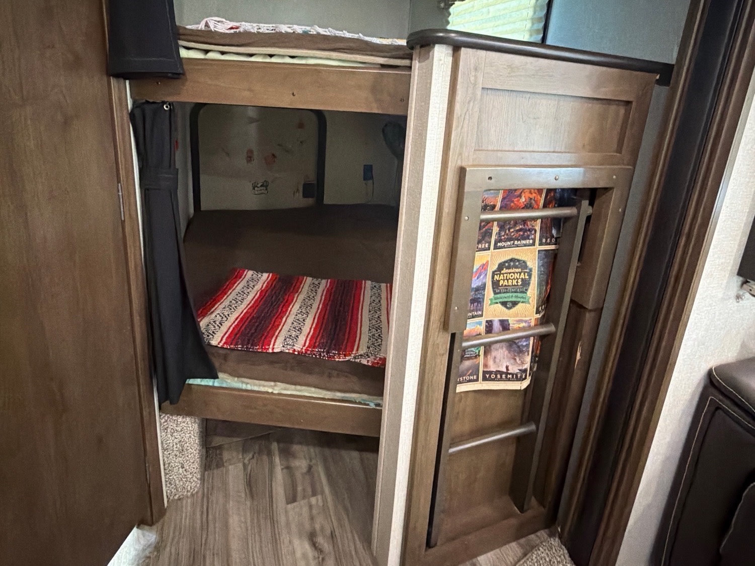 RV rental interior: bunk beds with a cozy blanket. A ladder displays National Parks guides, perfect for family adventures.. Keystone RV Cougar 2019