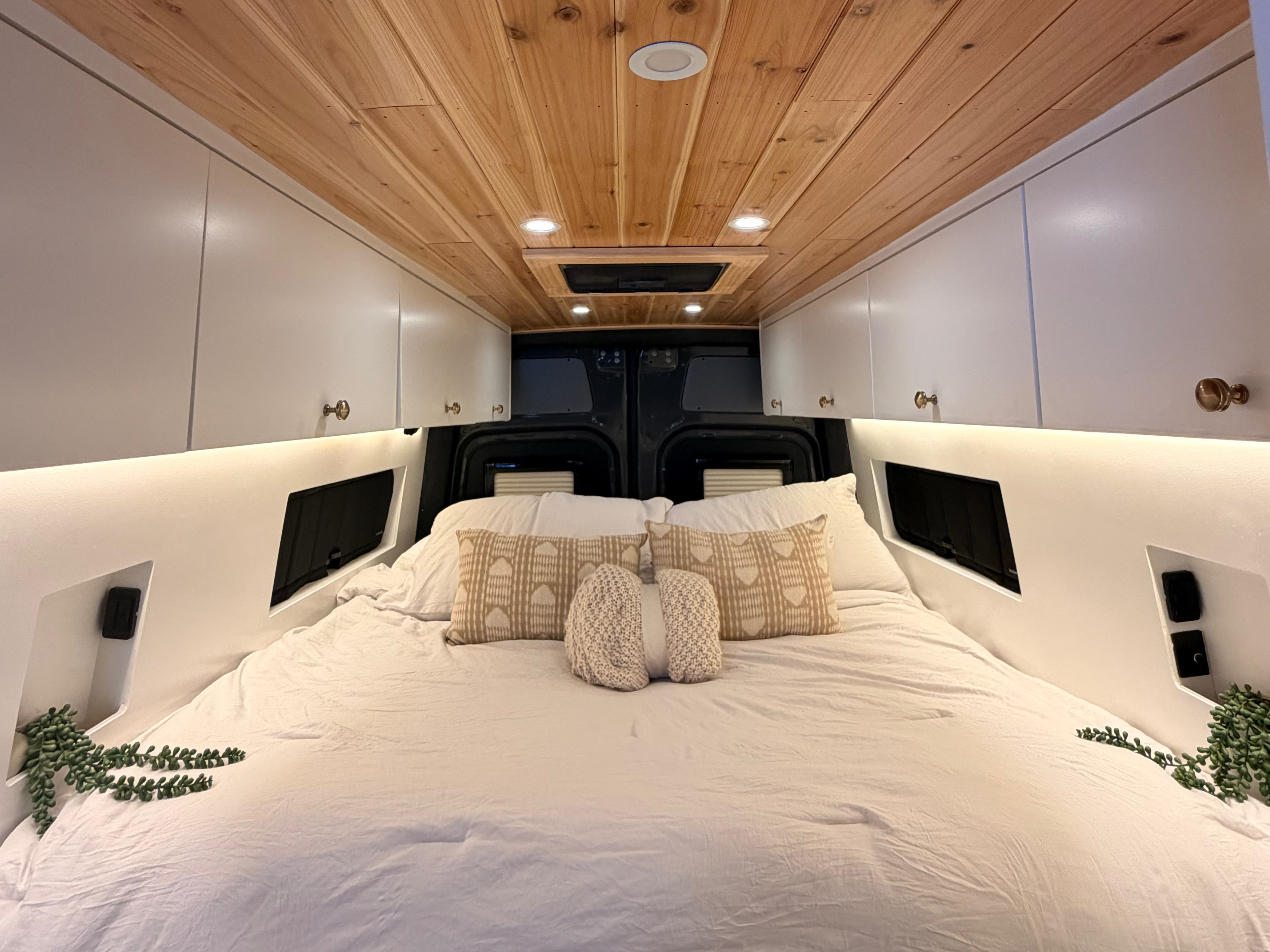Luxury RV rental bedroom: cozy bed, wood ceiling, sleek white cabinets, and bright ambient lighting for travel comfort.. Mercedes Sprinter 2025