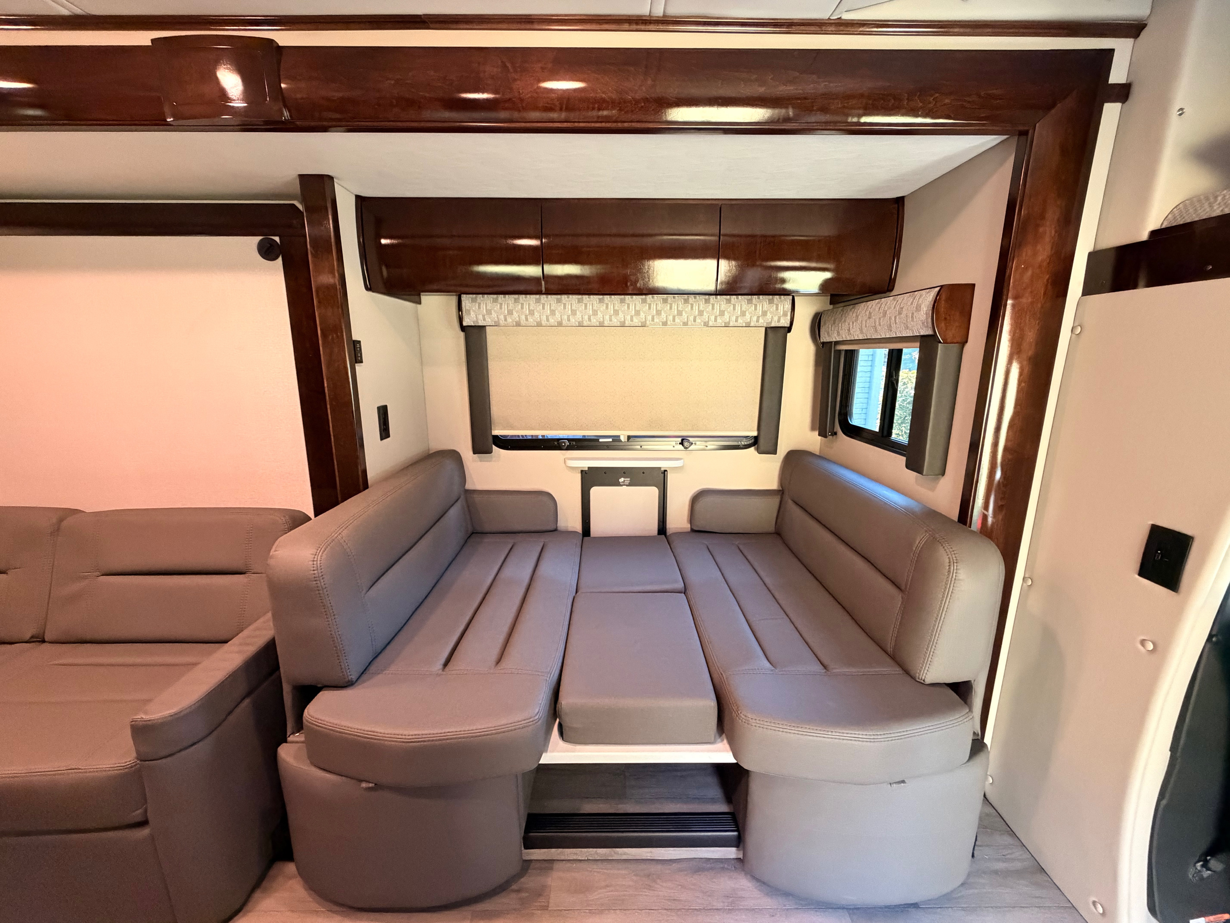 Inside an RV rental: a flexible dinette setup with two benches and a table that converts into a comfortable bed, surrounded by wood trim and windows.. Renegade Vienna 2024