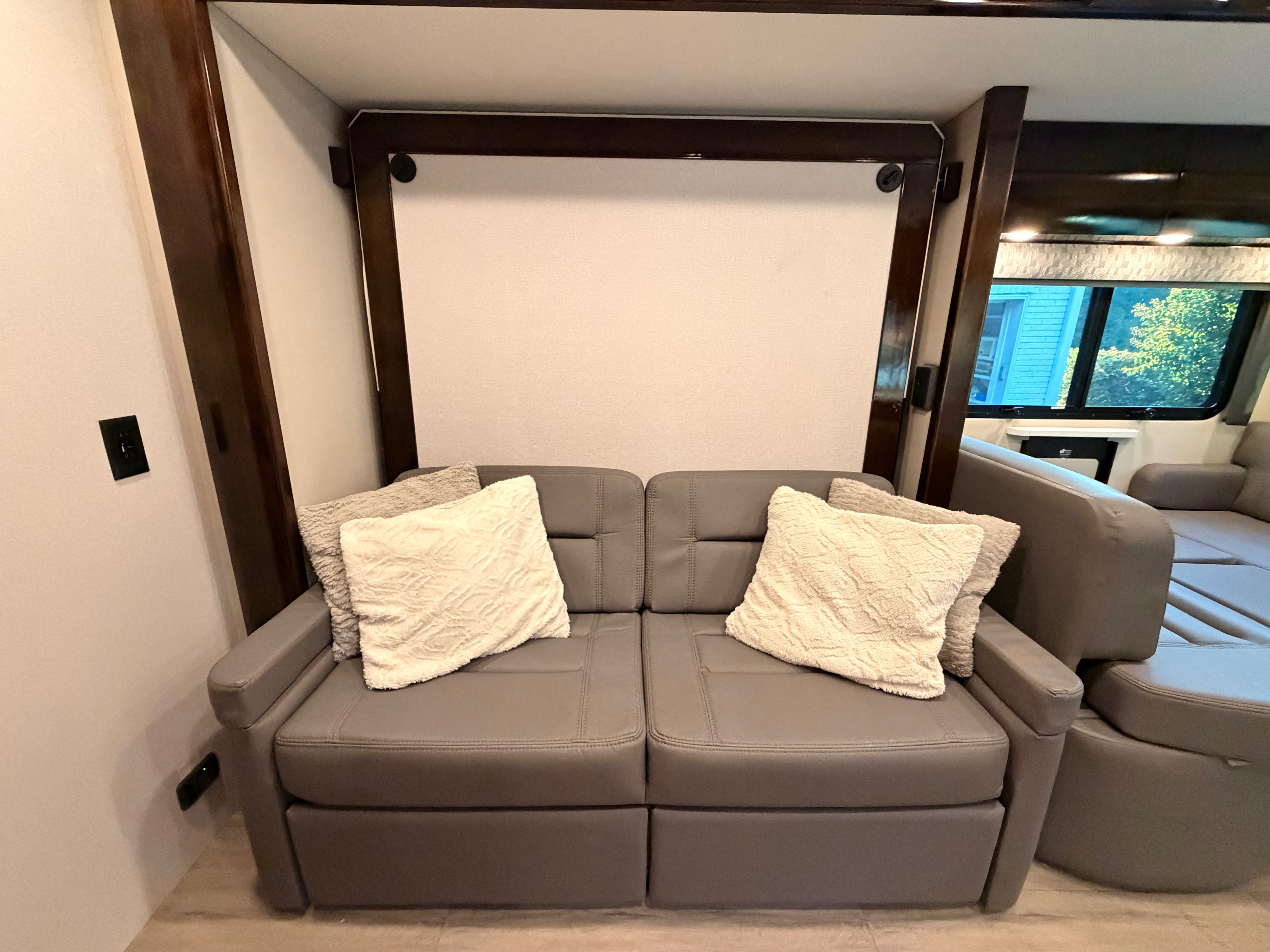 RV rental living space with a comfy gray sofa, accent pillows, and a space-saving wall bed system.. Renegade Vienna 2024