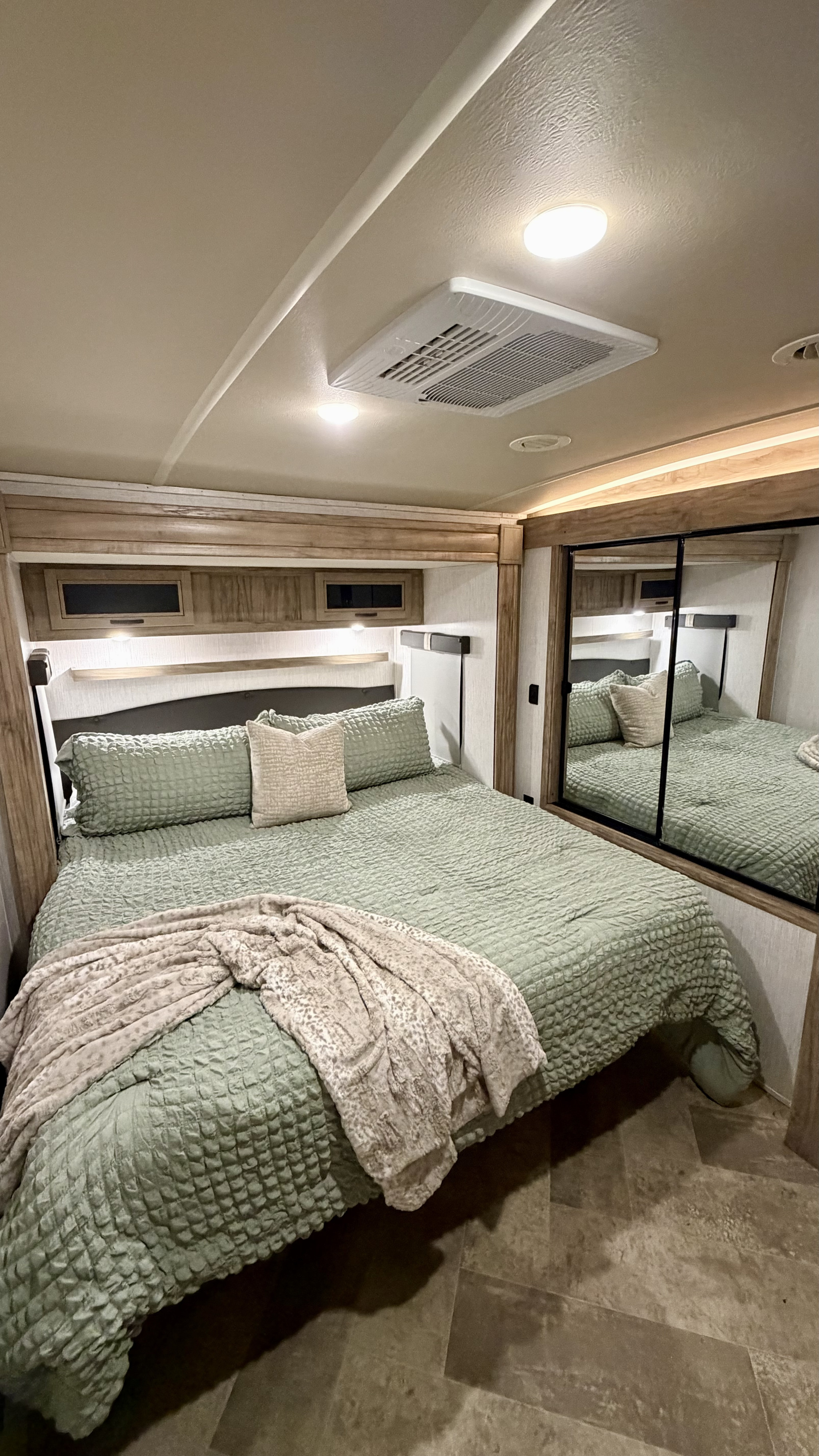 Experience comfort in this RV rental bedroom: large bed with sage green textured bedding, wood cabinets, and mirrored closet.. Forest River Palomino Solaire 2022