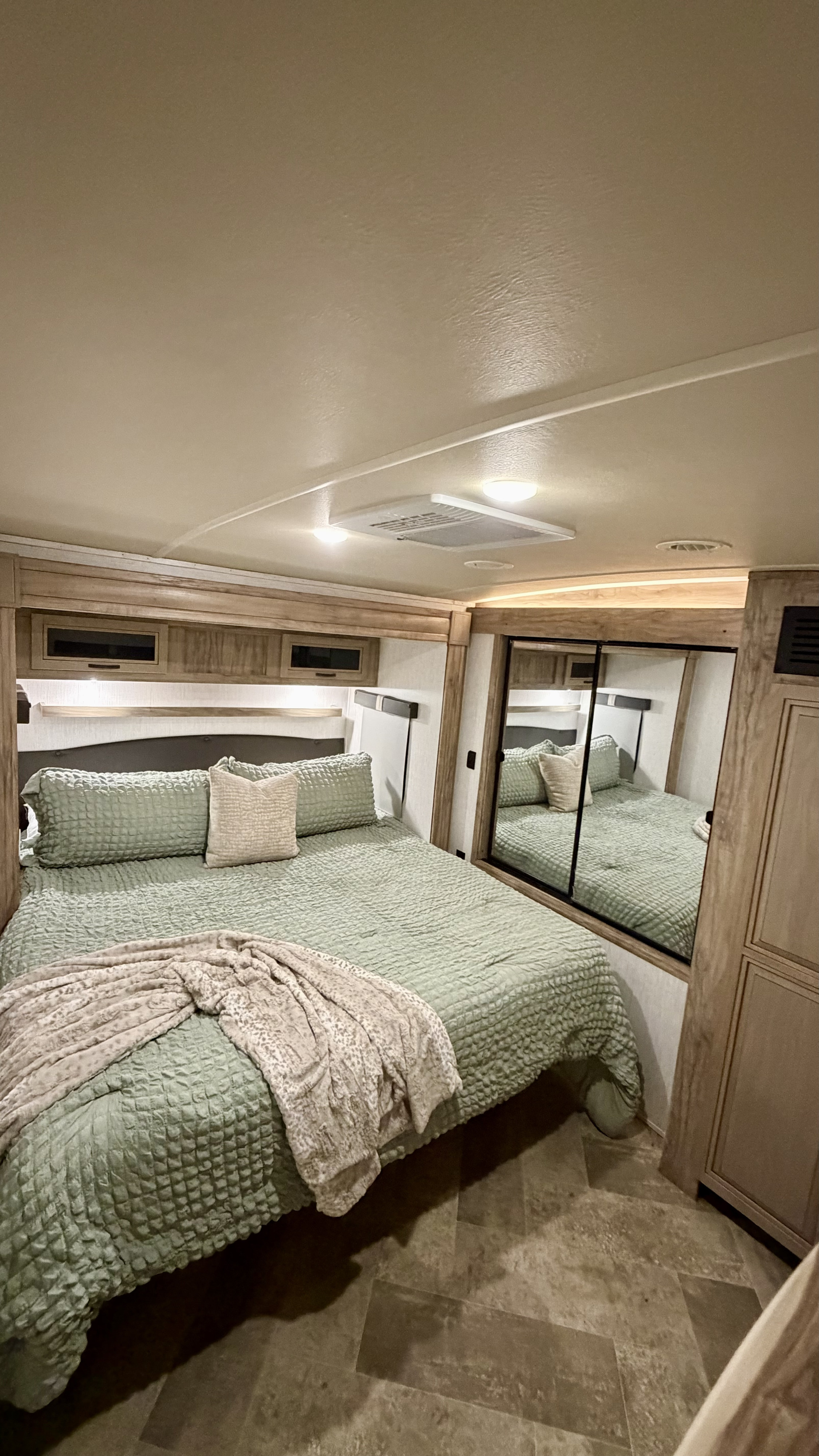 Comfortable RV rental bedroom featuring a large bed with green bedding, overhead storage, and mirrored closet doors.. Forest River Palomino Solaire 2022