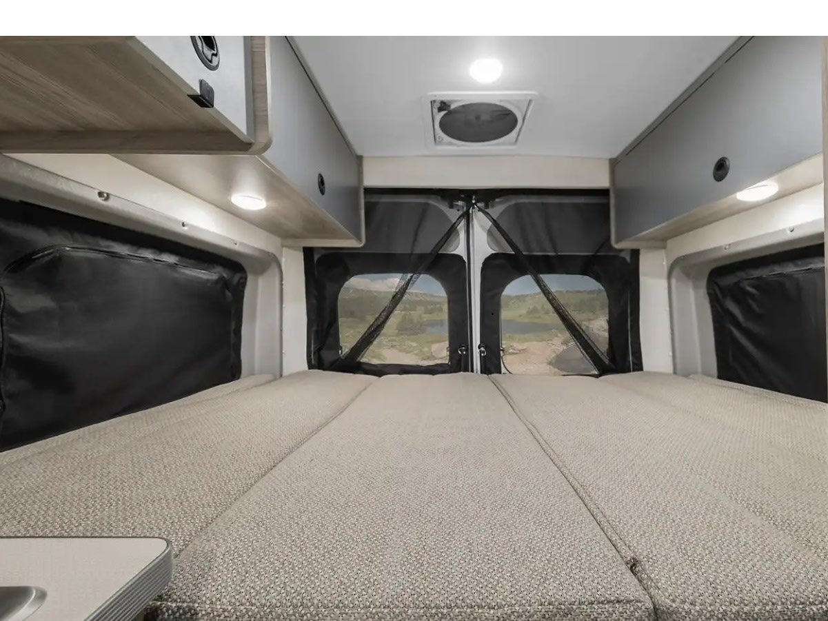 RV rental interior: A comfortable bed fills the space, with overhead cabinets and a scenic view through the mesh-screened rear doors.. Winnebago Solis 2021