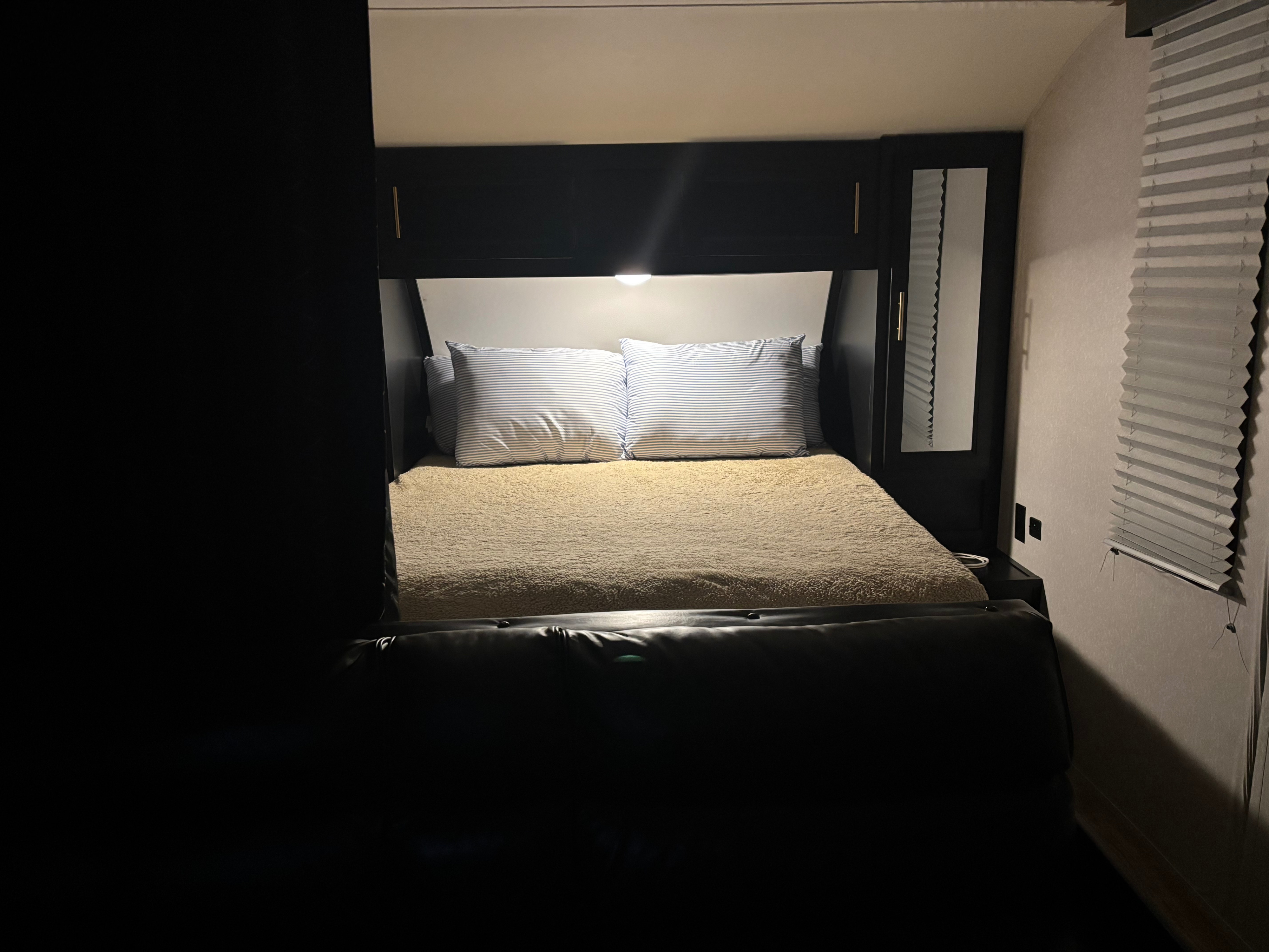 Cozy RV rental bedroom with bed, striped pillows, overhead cabinets & window blind. Dimly lit for a relaxing stay.. Forest River Cherokee Grey Wolf 2022