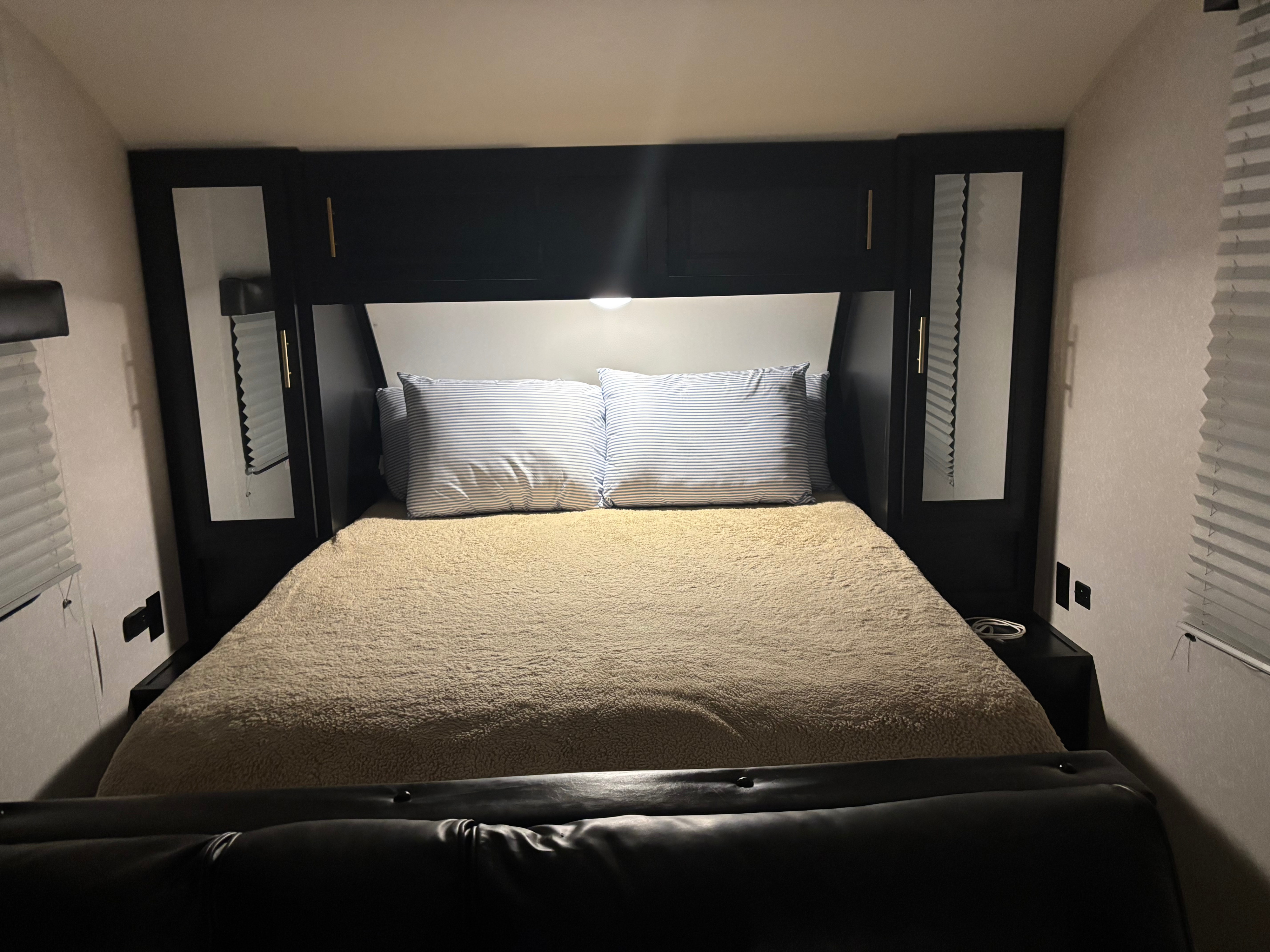 Cozy RV rental bedroom with a comfy bed, striped pillows, dark overhead storage, and soft lighting for a relaxing stay.. Forest River Cherokee Grey Wolf 2022