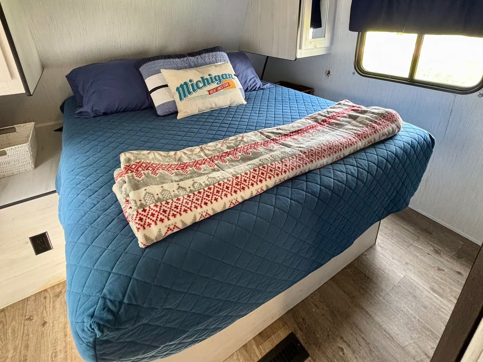 Cozy RV rental bedroom features a blue quilted bedspread, 'Michigan' pillow, and overhead storage. Ideal for travel.. Heartland RVs Trail Runner 2021