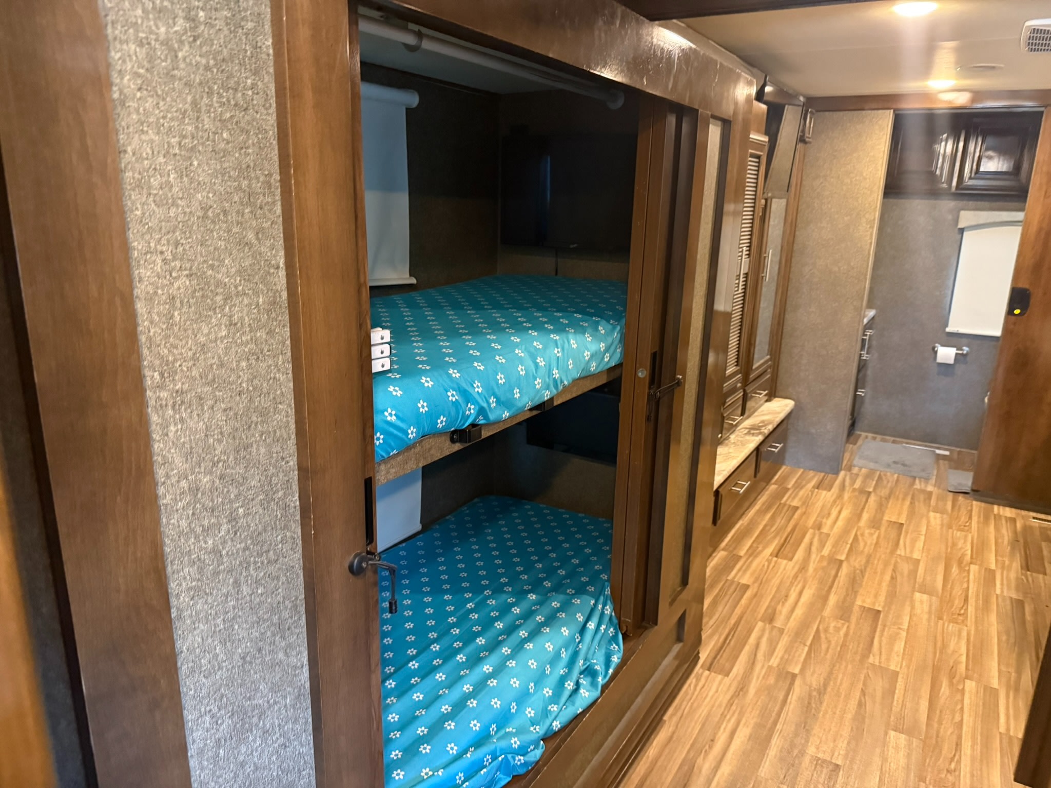 Inside an RV rental: two neatly made bunk beds with blue patterned sheets, wood-paneled walls, and flooring.. Thor Miramar 2019