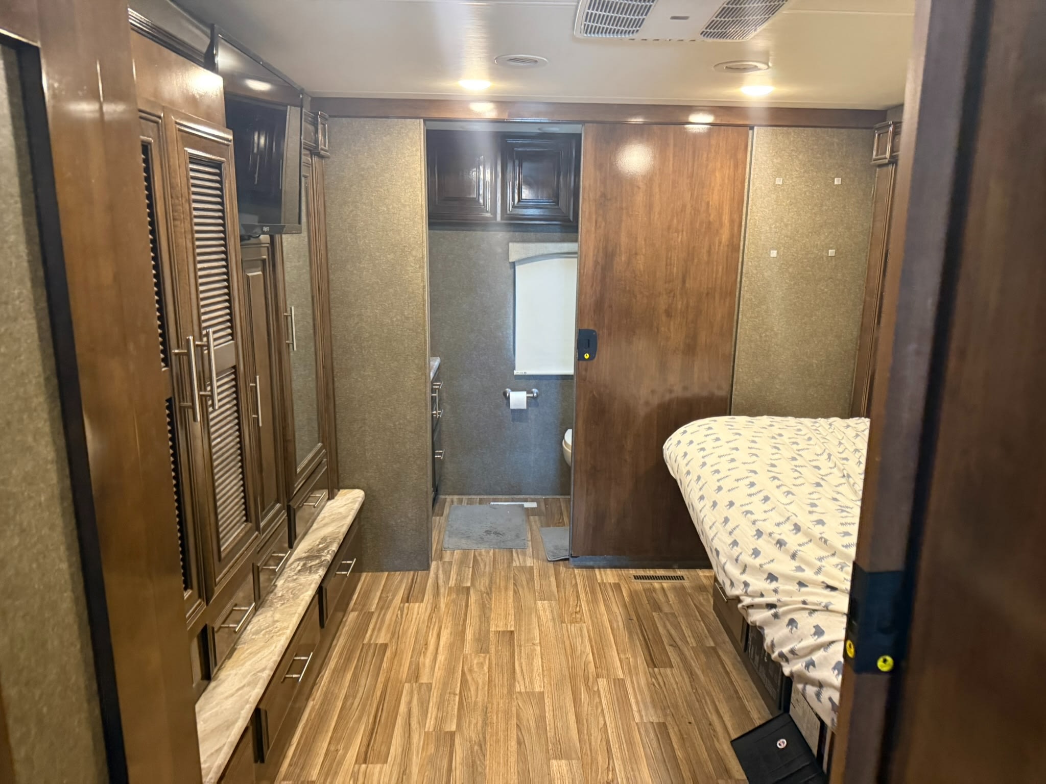 RV rental bedroom with sliding door to bathroom, large wardrobe, and TV. Features wood-look flooring and dark wood cabinetry.. Thor Miramar 2019