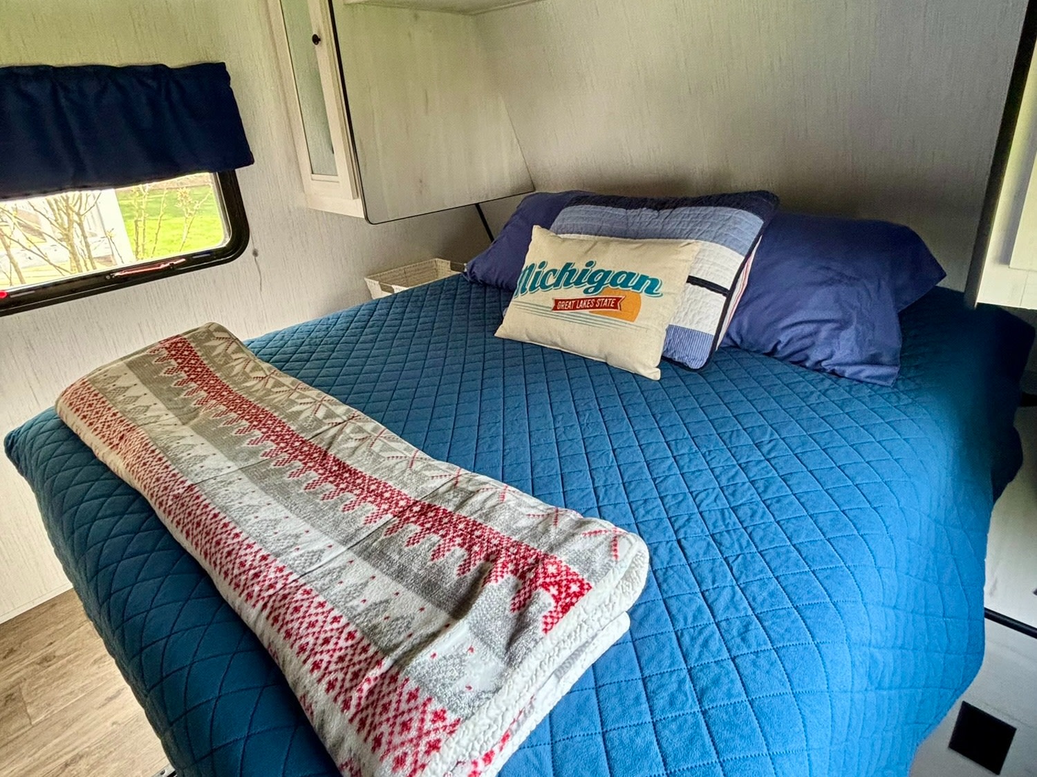Comfortable RV rental bedroom with blue bed, Michigan pillow, storage, & window. Ideal for travel adventures.. Heartland RVs Trail Runner 2021