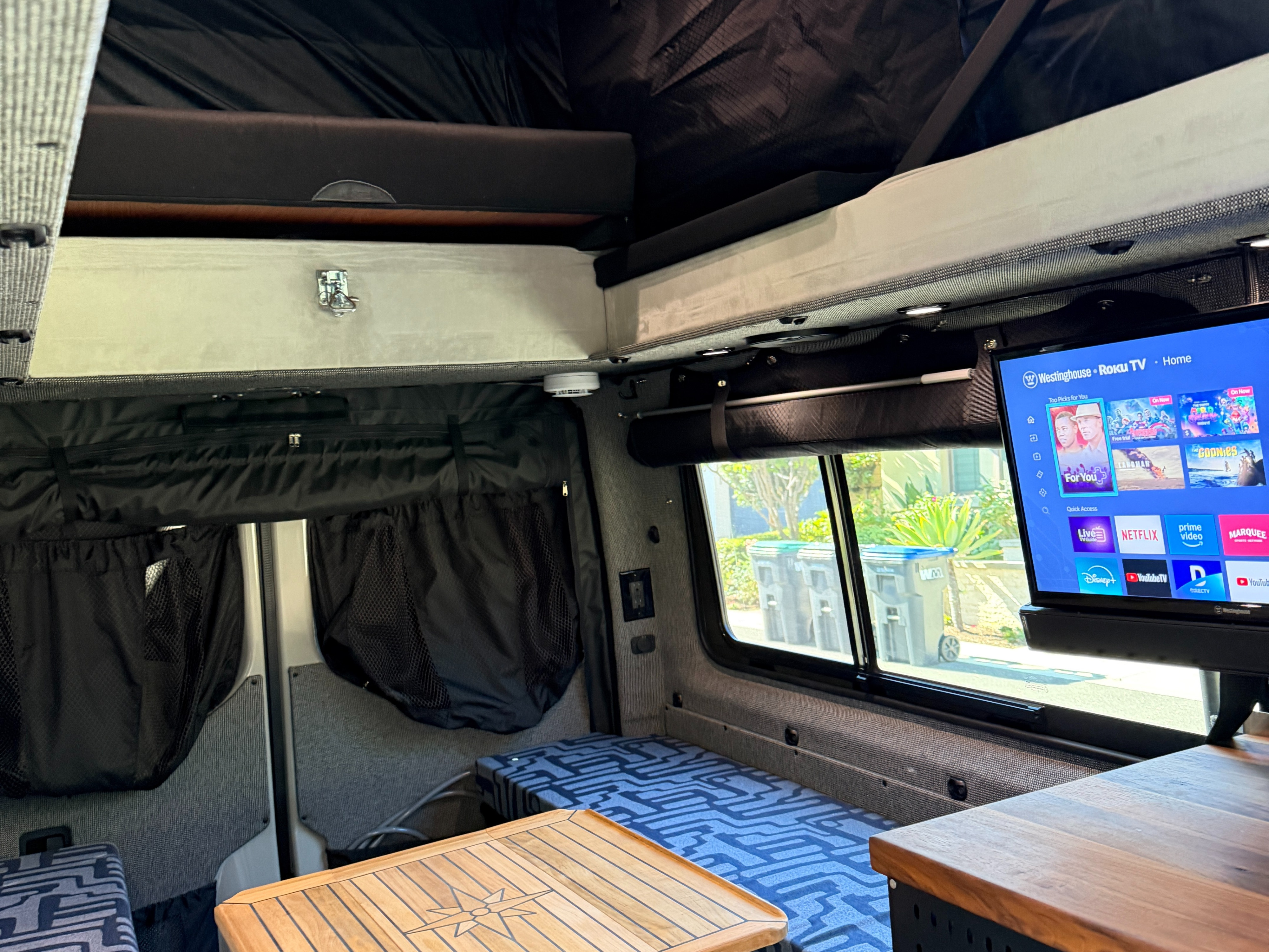 Cozy RV rental interior: upper bunk bed, lower patterned sleeping area, wood table, and Westinghouse Roku TV.. Exclusive Outfitters Model B 2026