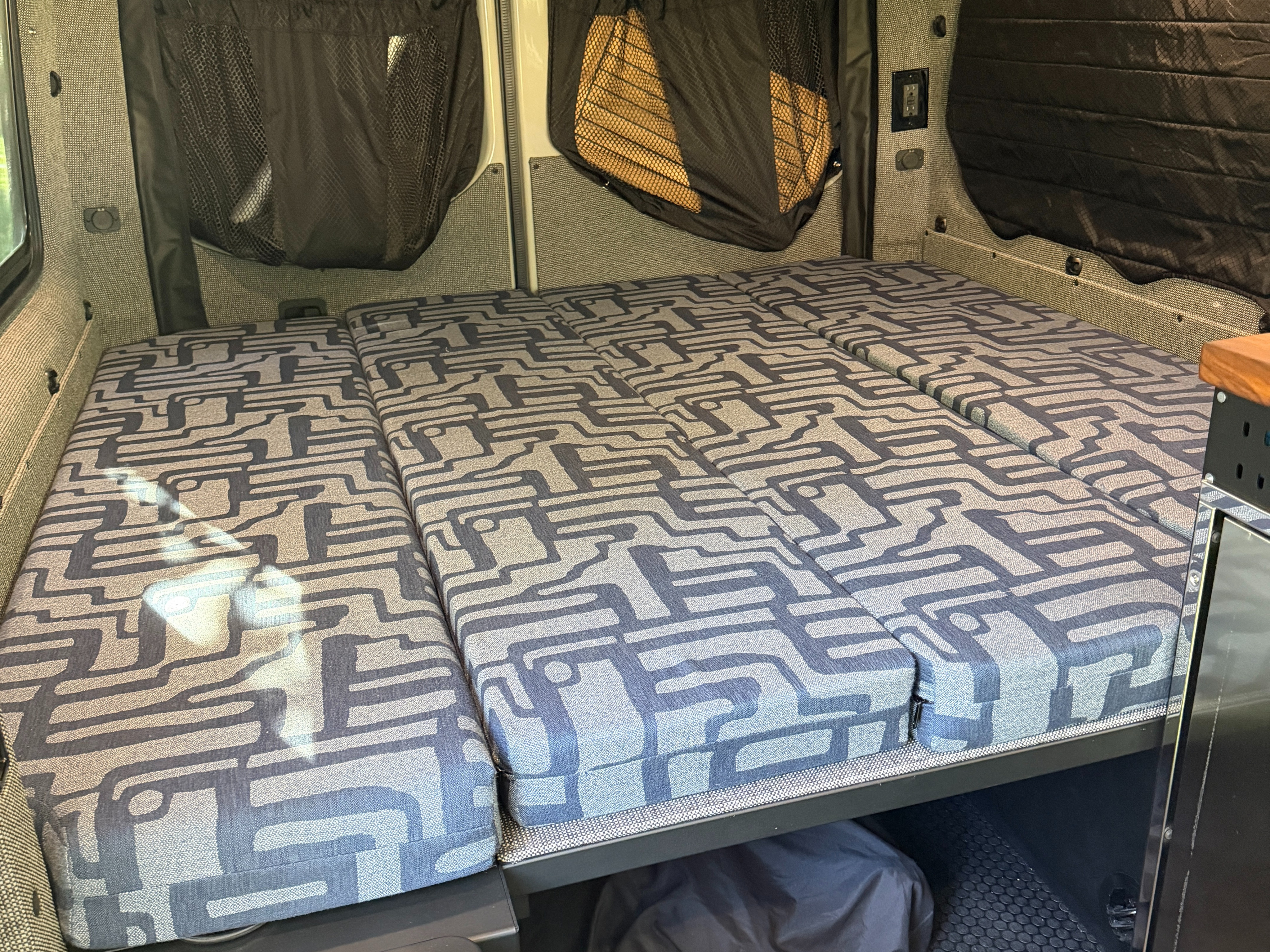 RV rental: Camper van's modular bed with geometric patterned cushions, mesh storage pockets, and charging outlets.. Exclusive Outfitters Model B 2026