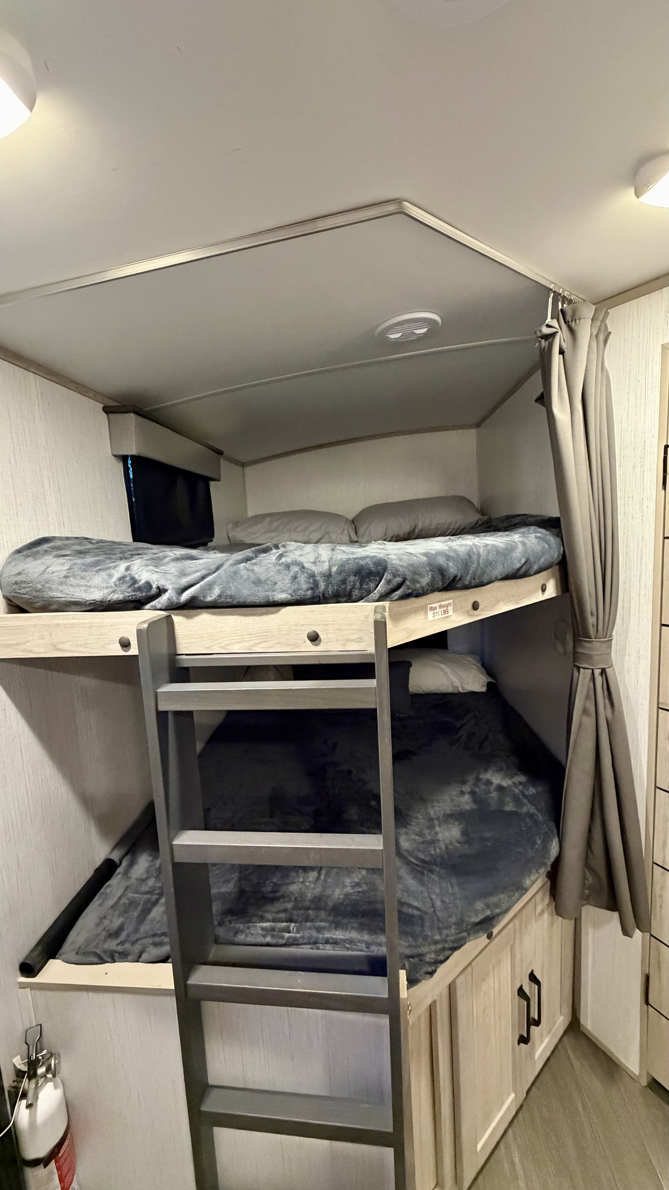 Interior of an RV rental showing bunk beds with grey bedding, a ladder, and a privacy curtain. A fire extinguisher is at the bottom left.. Heartland RVs Other 2022