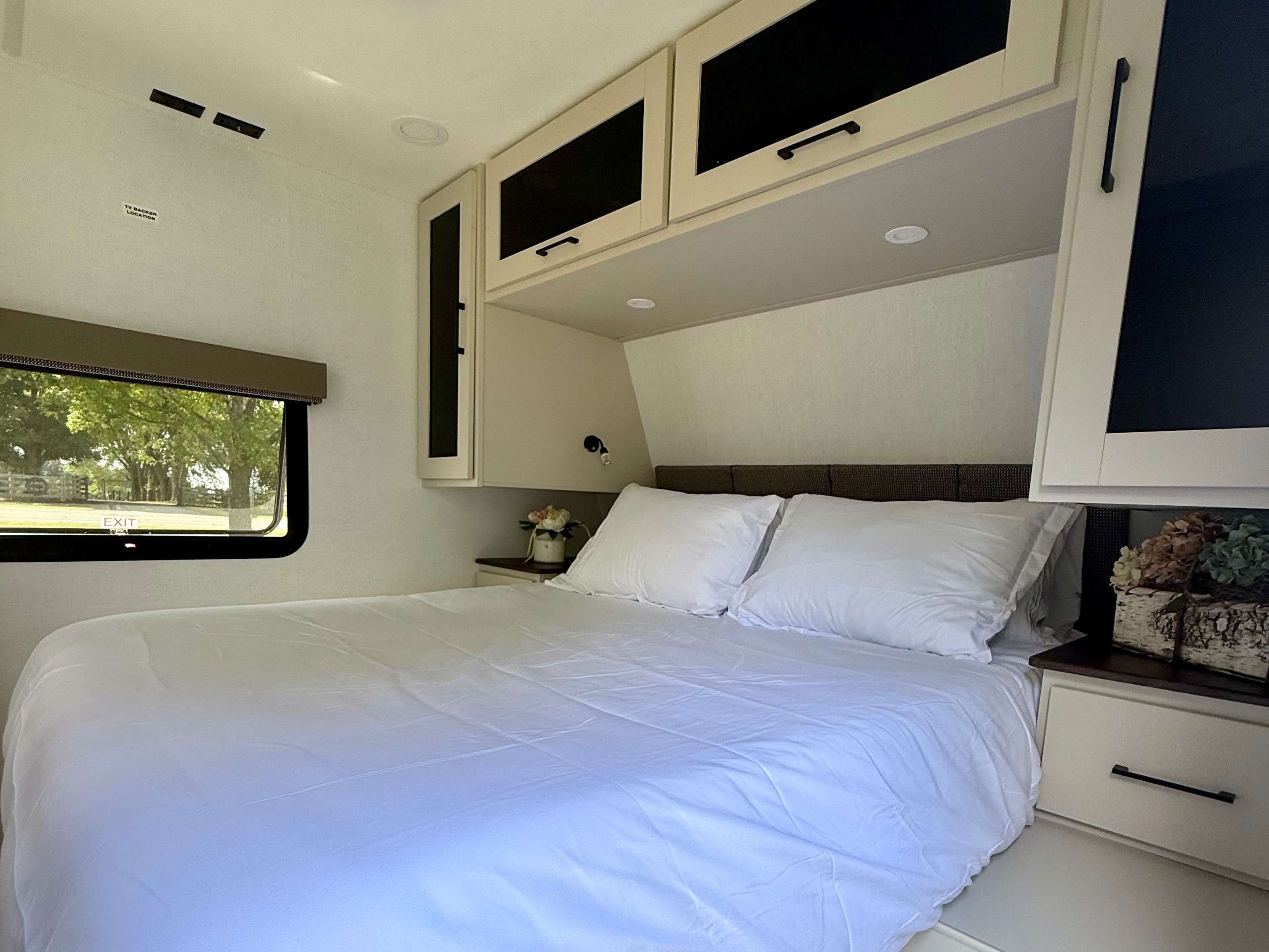 Bright and comfortable RV rental bedroom with a large bed, sleek overhead cabinets, and a scenic window view.. Alliance Delta 2027