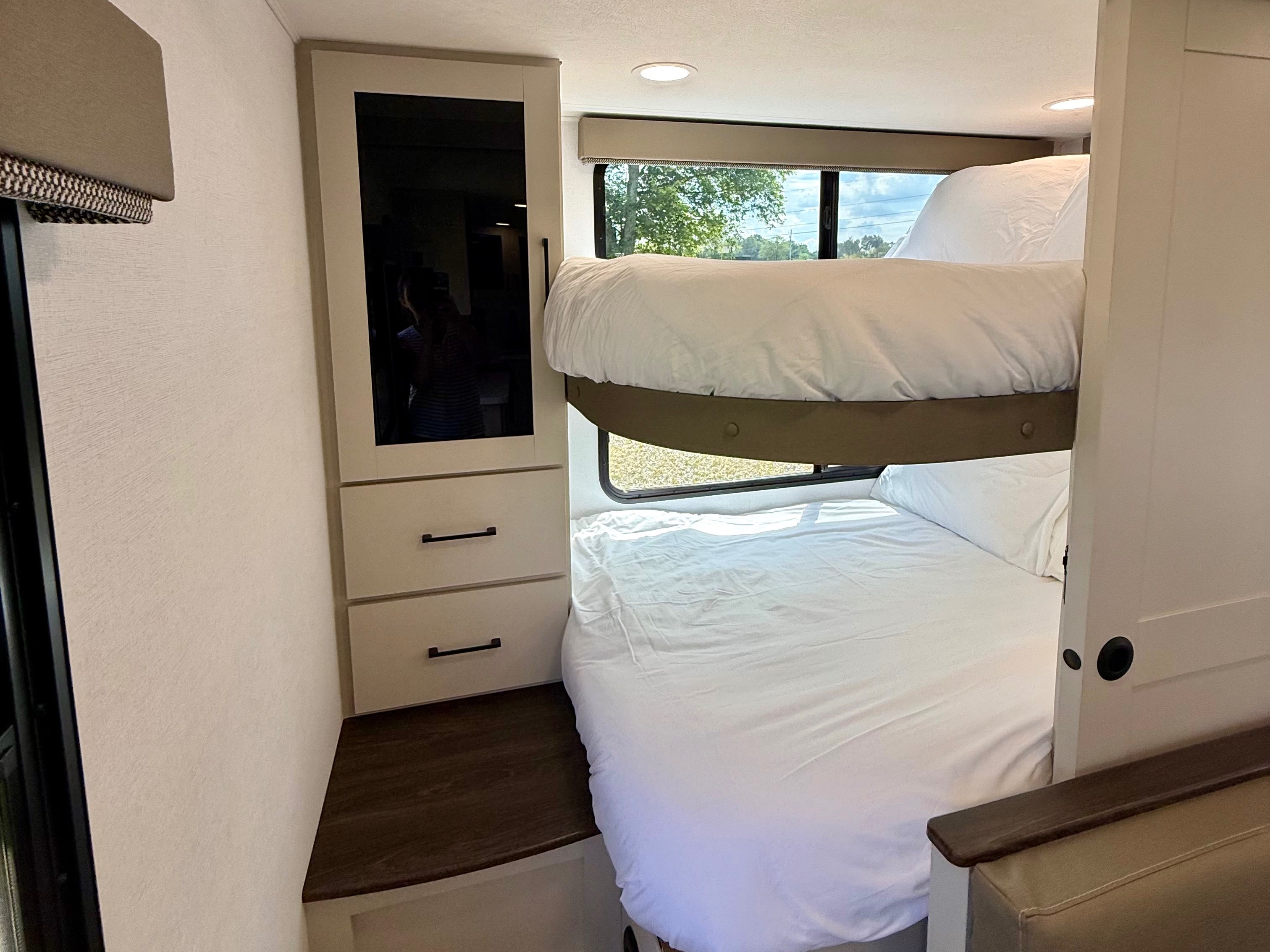 This RV rental bunk bed area features a mirrored wardrobe, drawers, and windows with white bedding for comfort.. Alliance Delta 2027