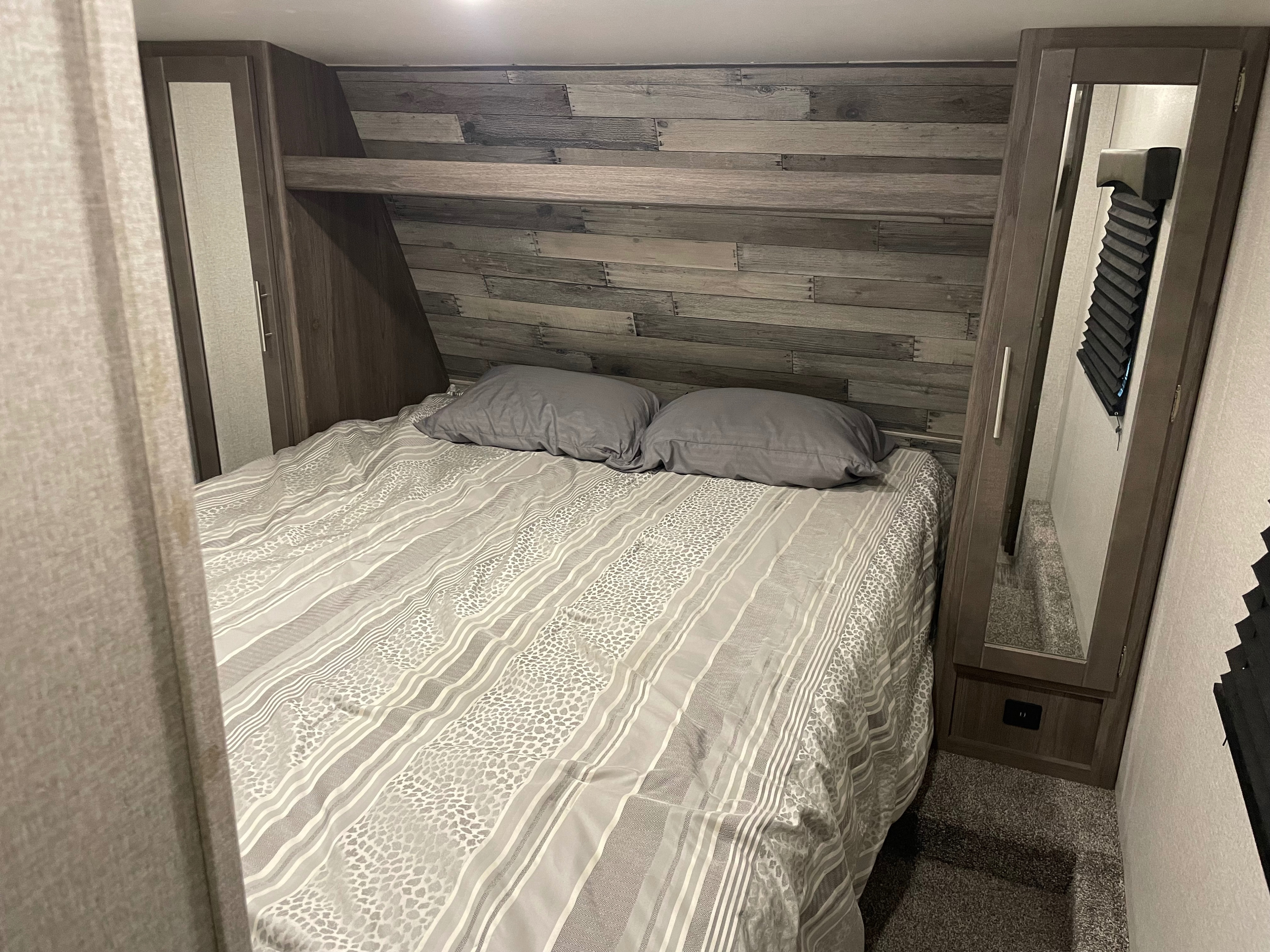 Cozy RV rental bedroom with a grey-patterned bed, built-in storage, and a stylish wooden accent wall for compact comfort.. Crossroads RV Volante 2021