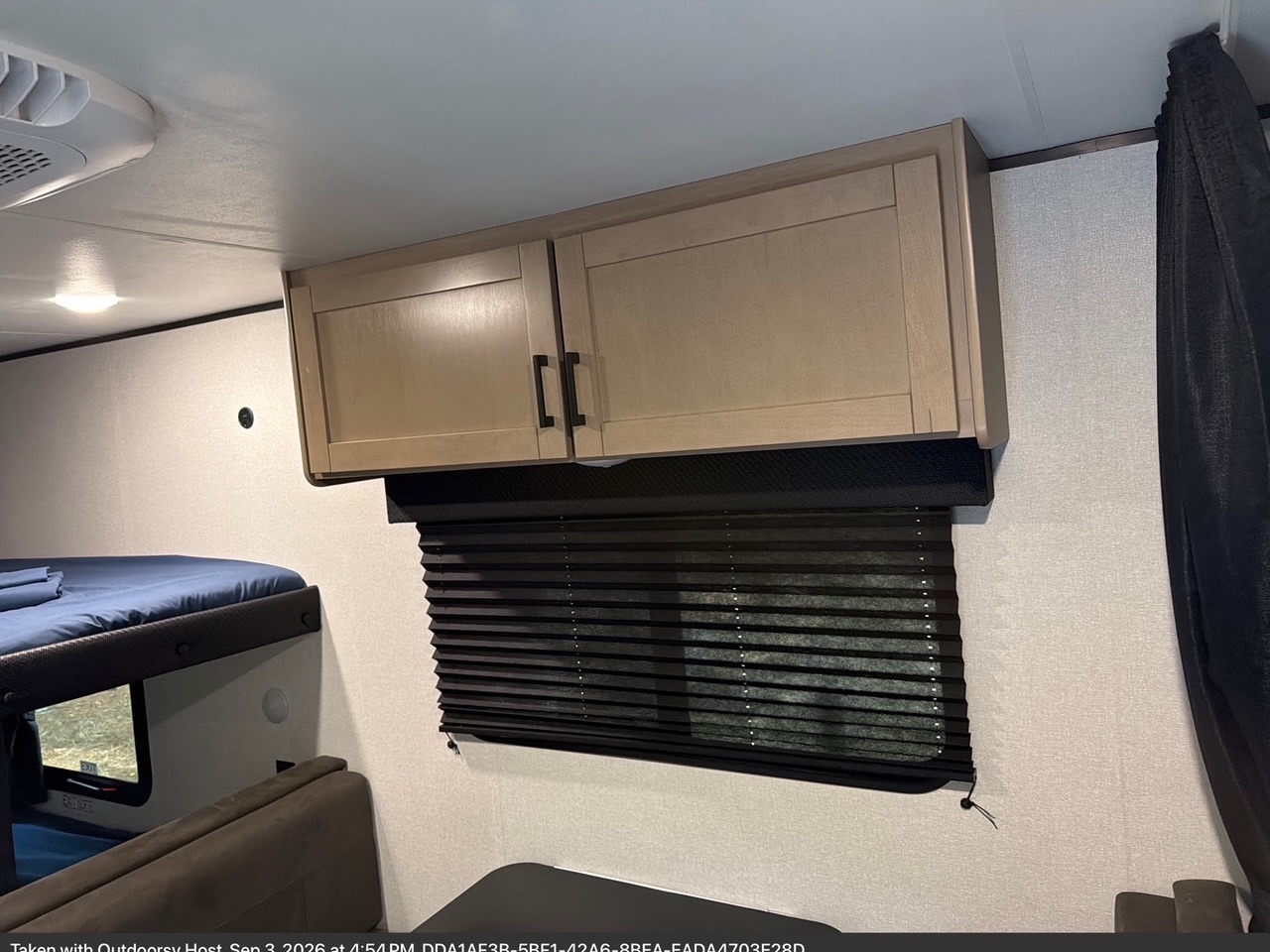 RV rental interior featuring light wood overhead cabinets, a black pleated window blind, and a cozy bunk bed with blue sheets.. Jayco Jay Flight SLX 2026
