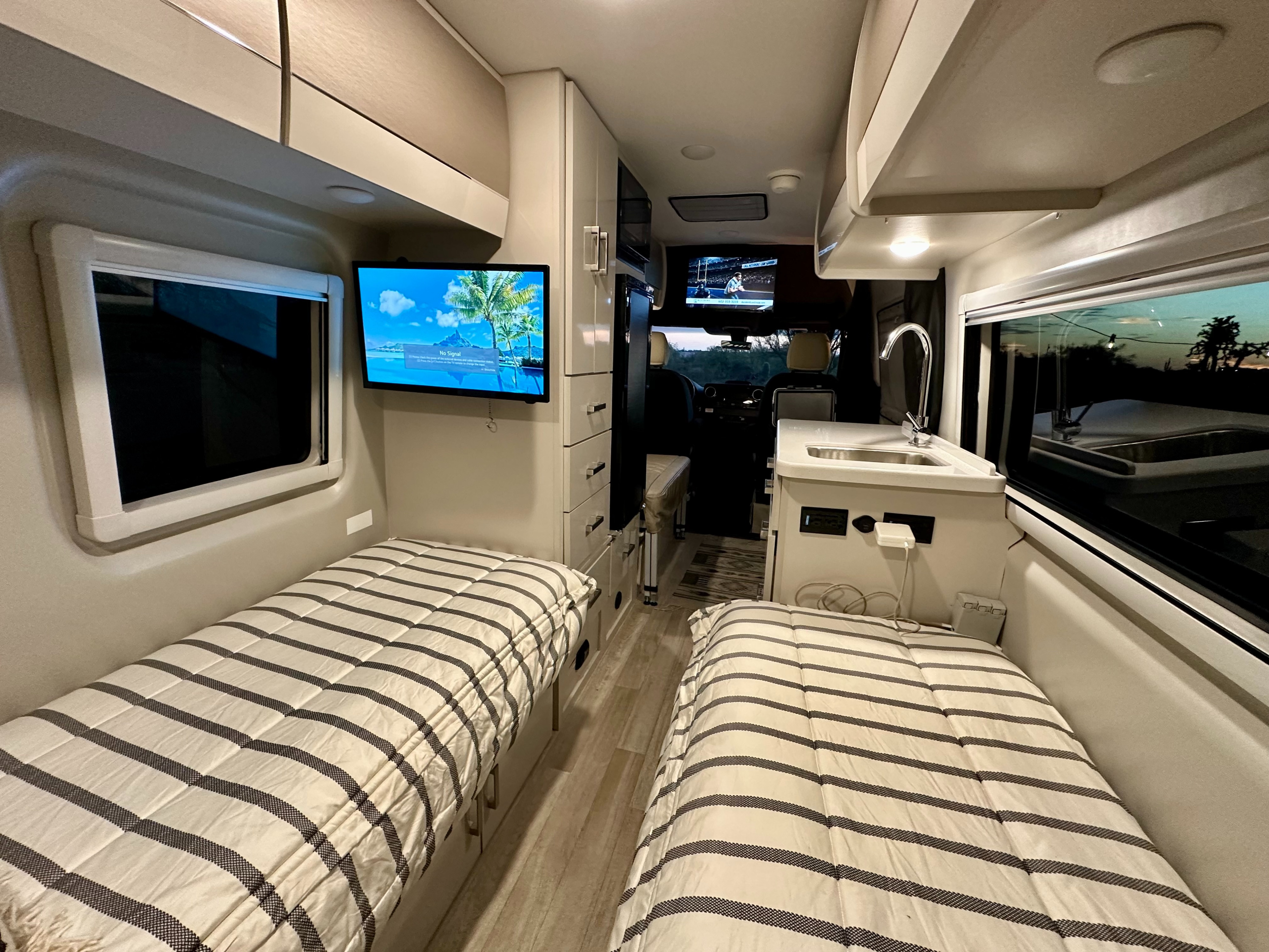 Cozy rv rental interior featuring twin beds, two TVs, a sink, and cabinet storage, perfect for a comfortable road trip.. Thor Tranquility 2026
