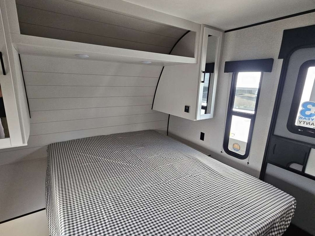 Modern RV rental bedroom: comfy checkered bed, white shiplap wall, overhead storage, and window. Ideal for travel.. Jayco Jay Flight SLX 2026