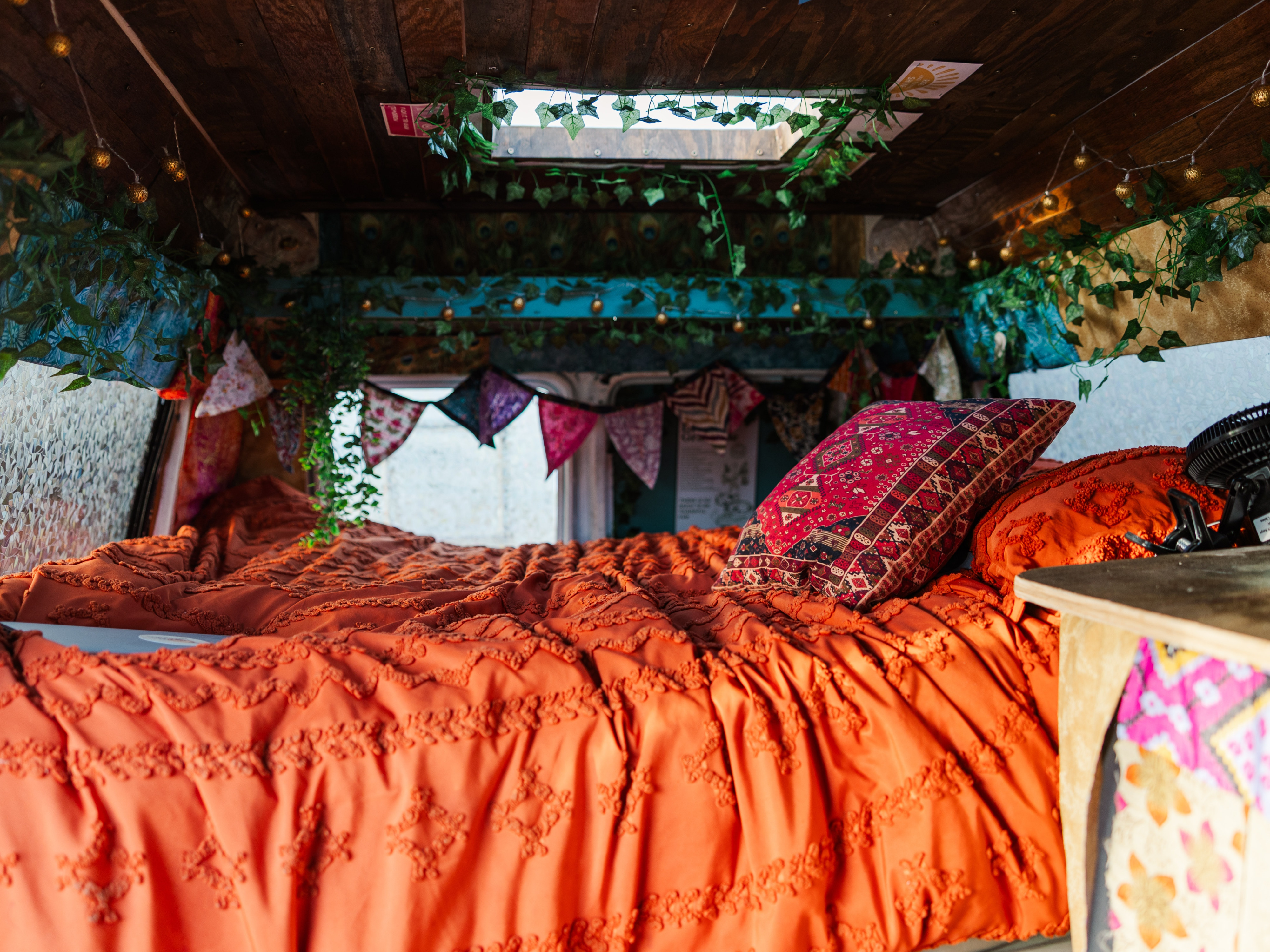 Bright and cozy rv rental bed with a textured orange comforter, patterned pillow, and ambient string lights inside a decorated van.. Dodge Ram 1500 2000