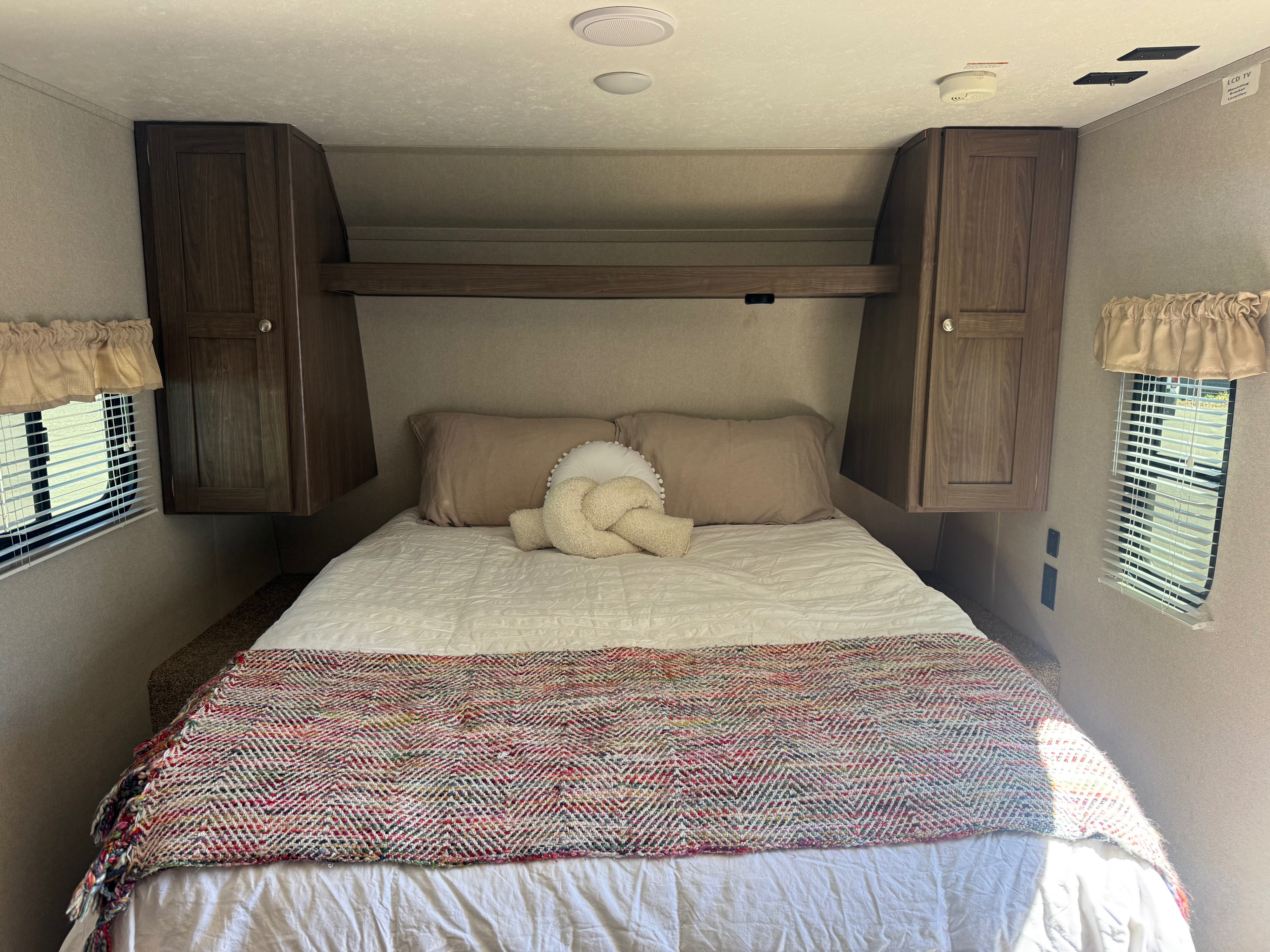 Inviting RV rental bedroom with a cozy bed, ample overhead storage, and natural light from windows. Ready for rest!. Keystone RV Hideout 2020