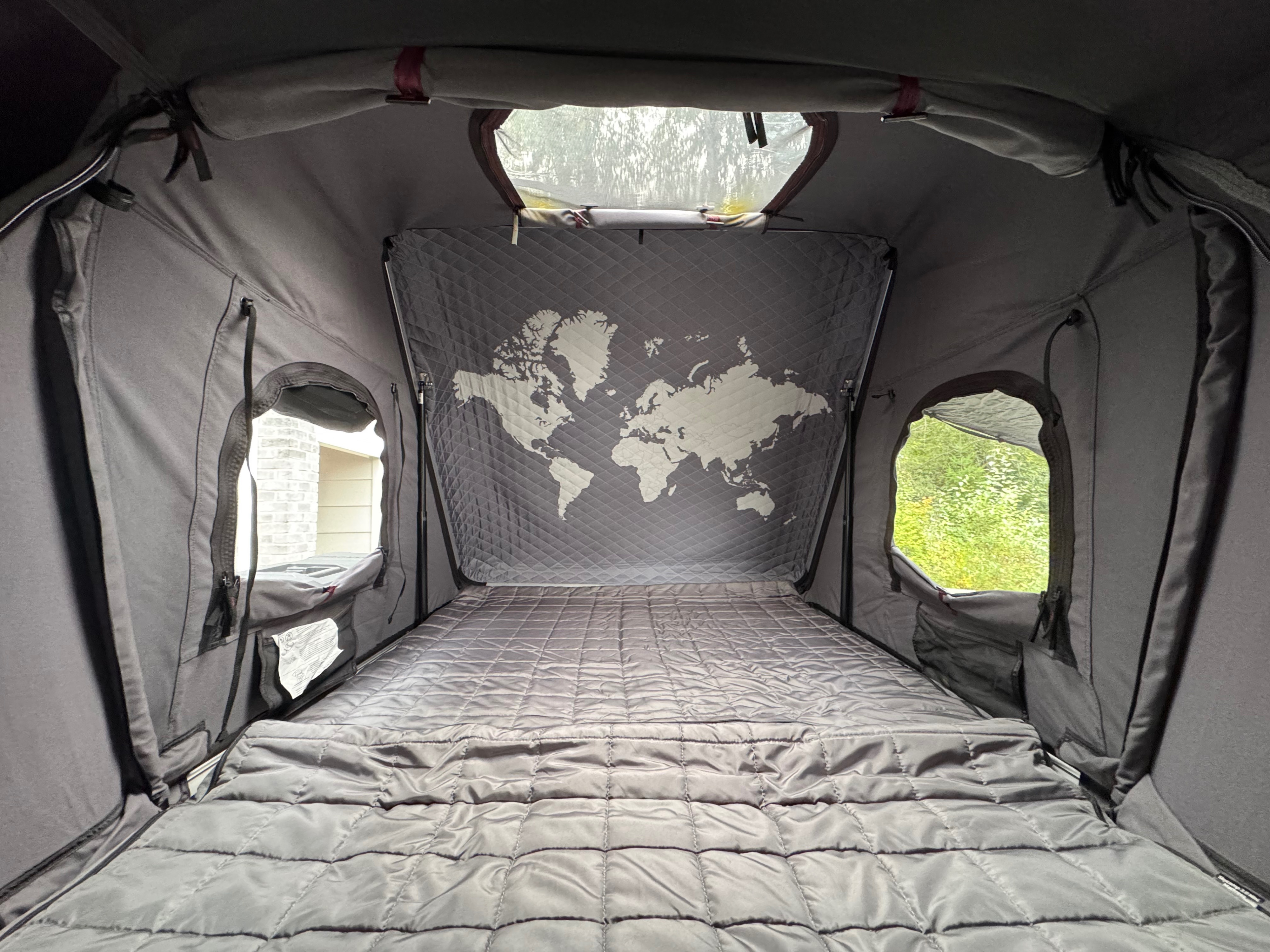 Interior of a cozy, quilted roof-top tent with a world map wall and open windows, ideal for an rv rental adventure.. Jeep Wrangler Rubicon Unlimited 2021