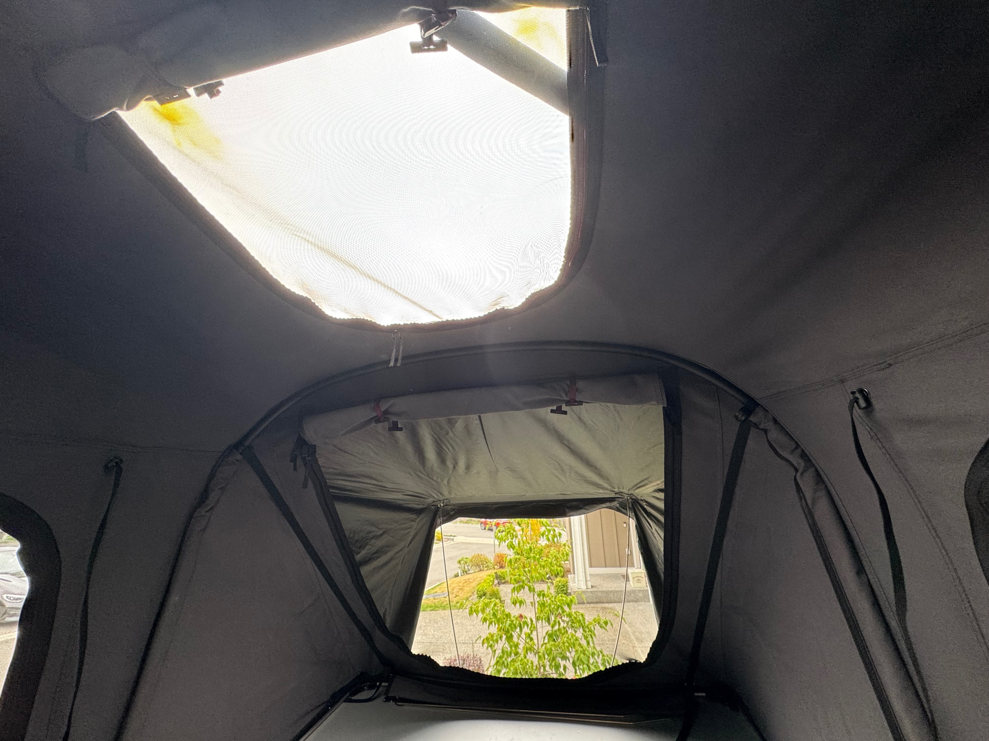 Interior of an RV rental rooftop tent, featuring a bright skylight with yellow stains & an open window view to the outside.. Jeep Wrangler Rubicon Unlimited 2021