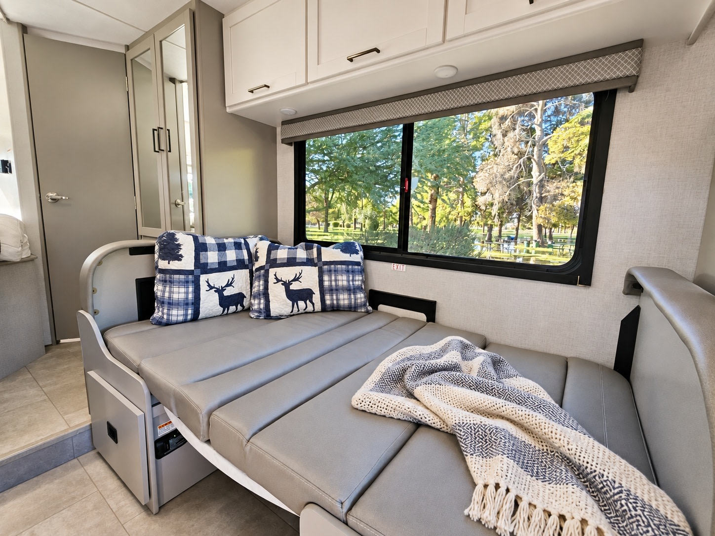 Cozy RV rental interior featuring a comfortable bed with plaid pillows, a throw blanket, and a scenic window view.. Thor Chateau 2026