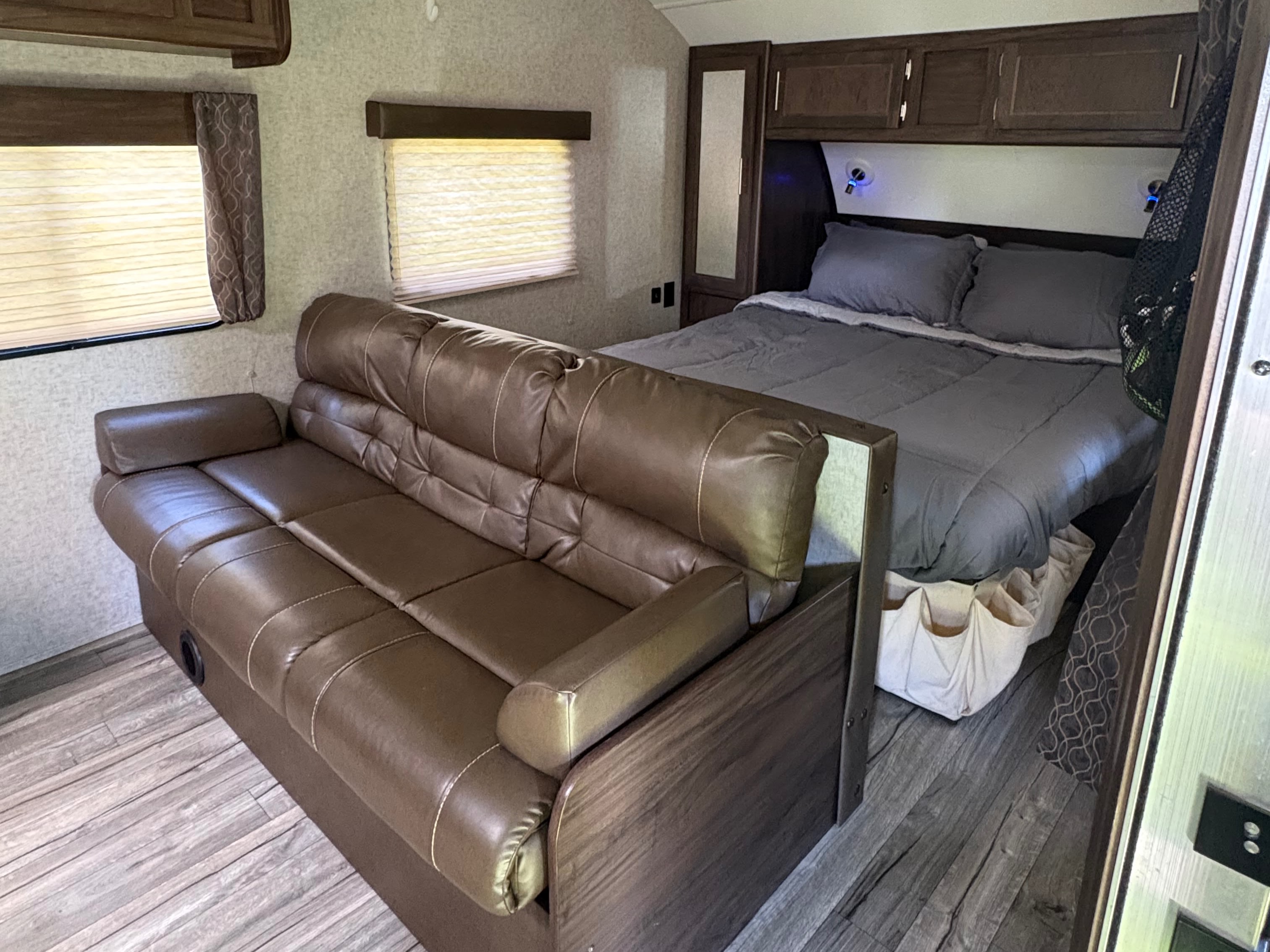 Inside this RV rental: a brown faux leather sofa and a bed with gray bedding, flanked by windows and cabinets.. Forest River Cherokee Grey Wolf 2018