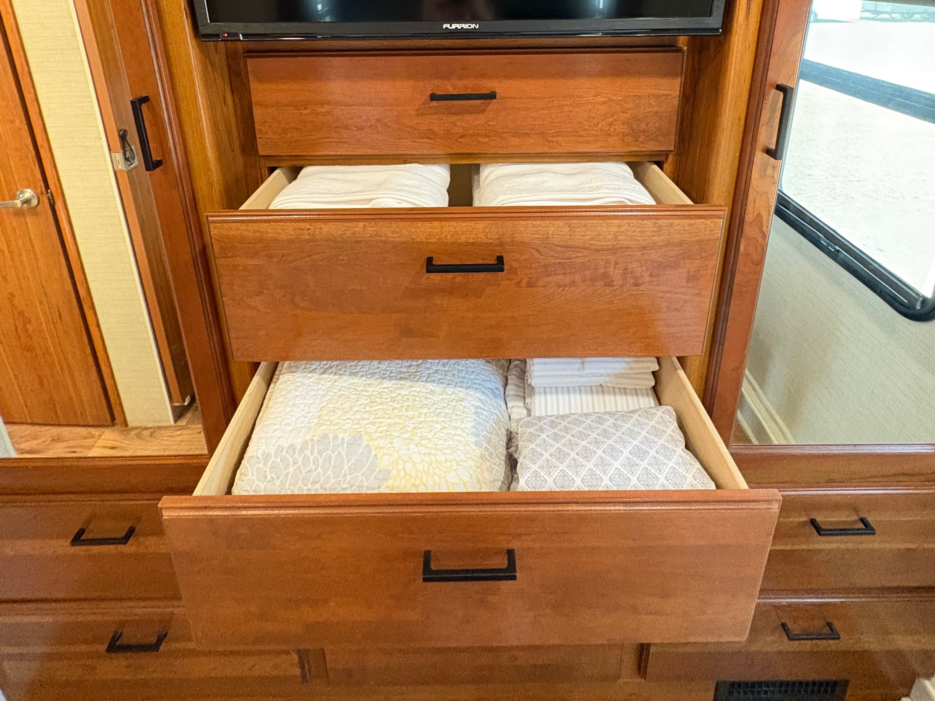 Neat RV rental bedroom storage: TV, and open wooden drawers with folded linens and bedding for convenient interior living.. Jayco Precept 2017