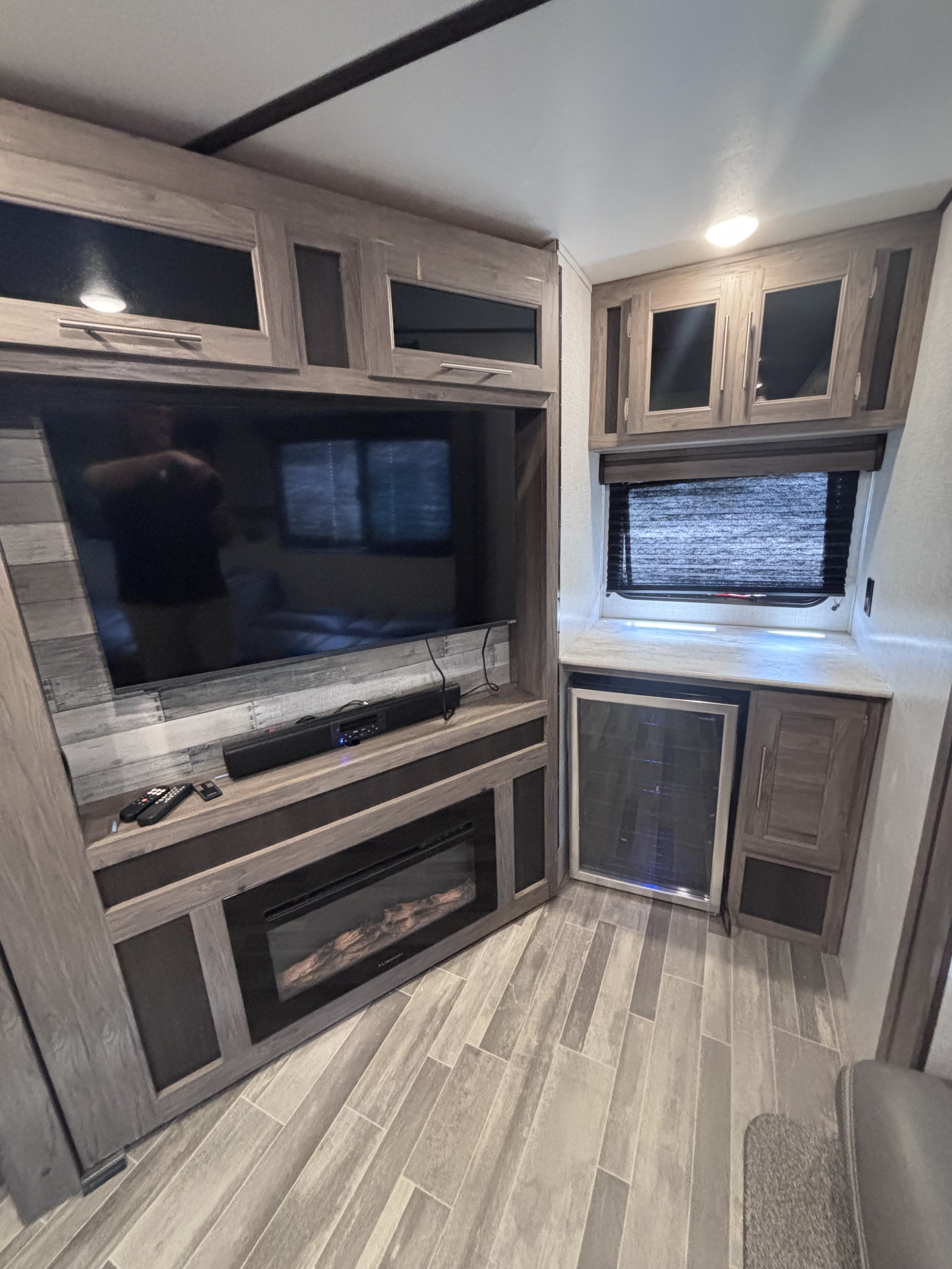 Interior of a modern RV rental featuring a large TV, electric fireplace, built-in mini-fridge, and overhead storage.. Crossroads RV Zinger 2021