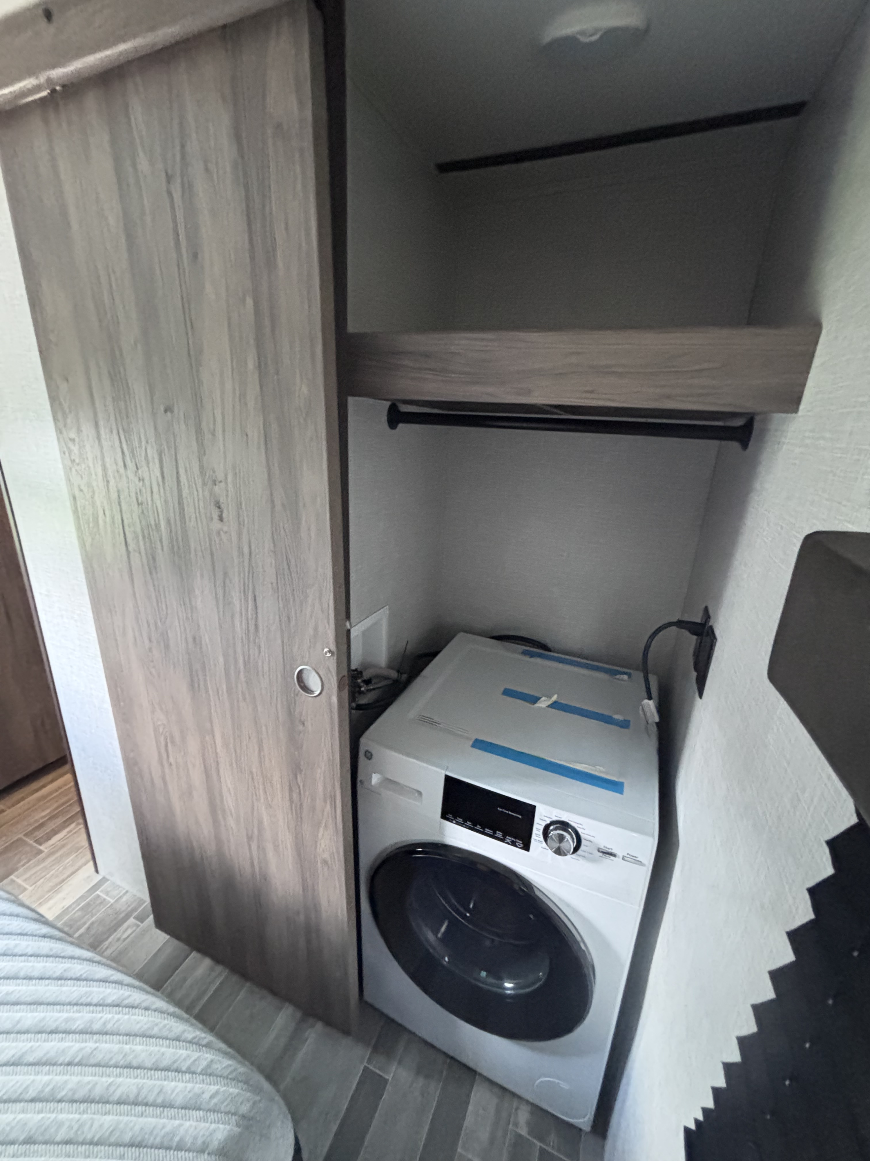 Inside an RV rental: a compact white washing machine is installed in a closet, with a shelf & hanging rod above.. Crossroads RV Zinger 2021