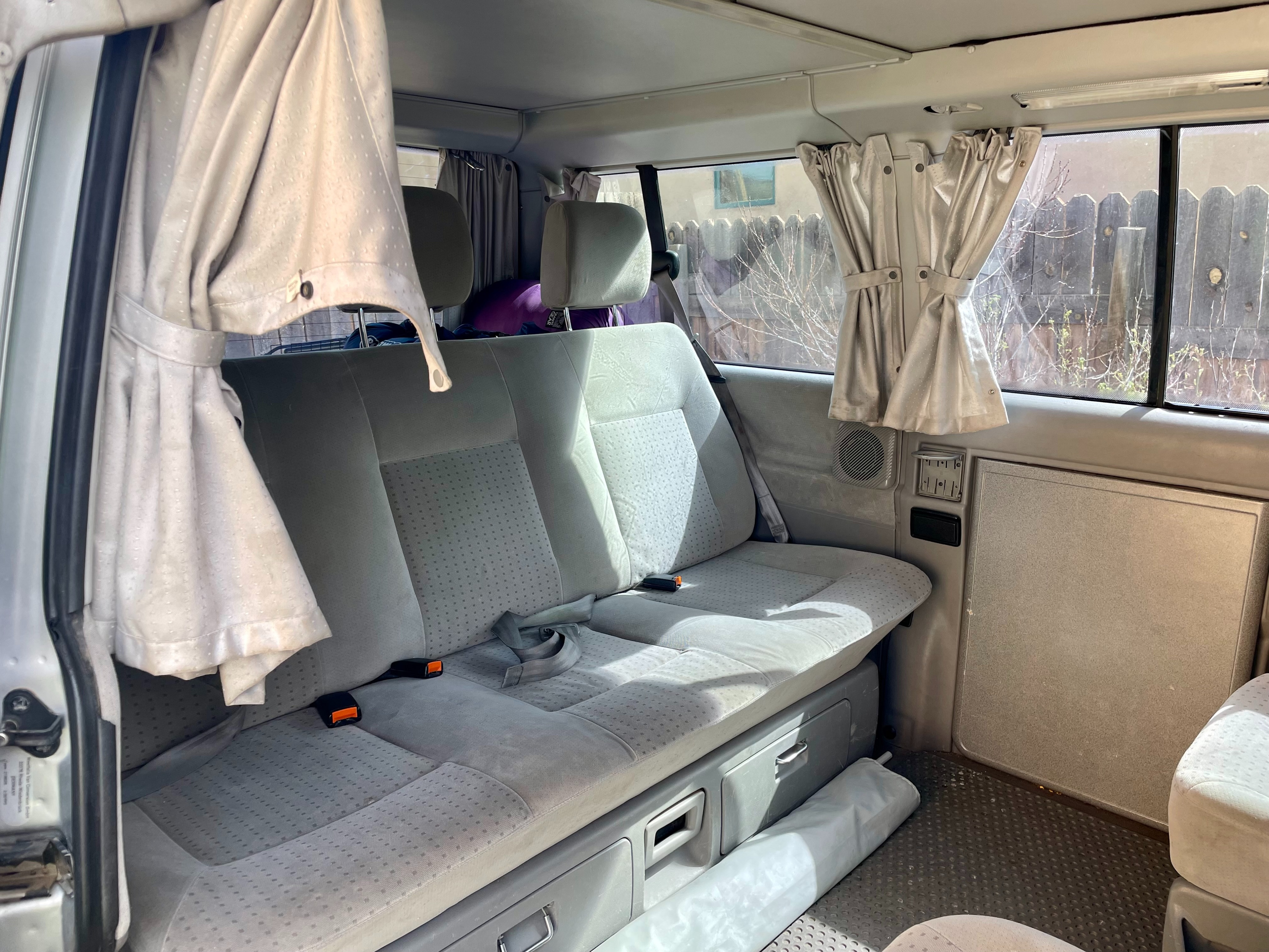 RV rental interior: light gray rear bench seat with storage below, and tied-back window curtains create a cozy camper experience.. Eurovan Camper Eurovan Camper Class B 2002