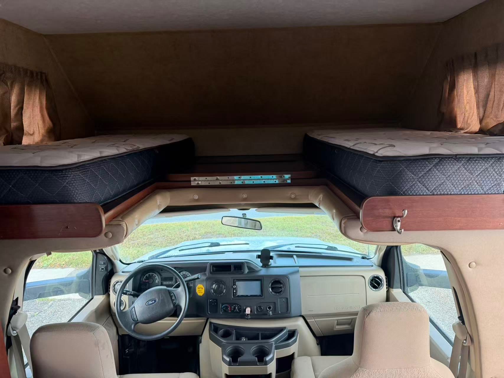 RV rental interior: Front cockpit with steering wheel and dashboard, below an overhead bunk bed with two mattresses.. Forest River Sunseeker 2017
