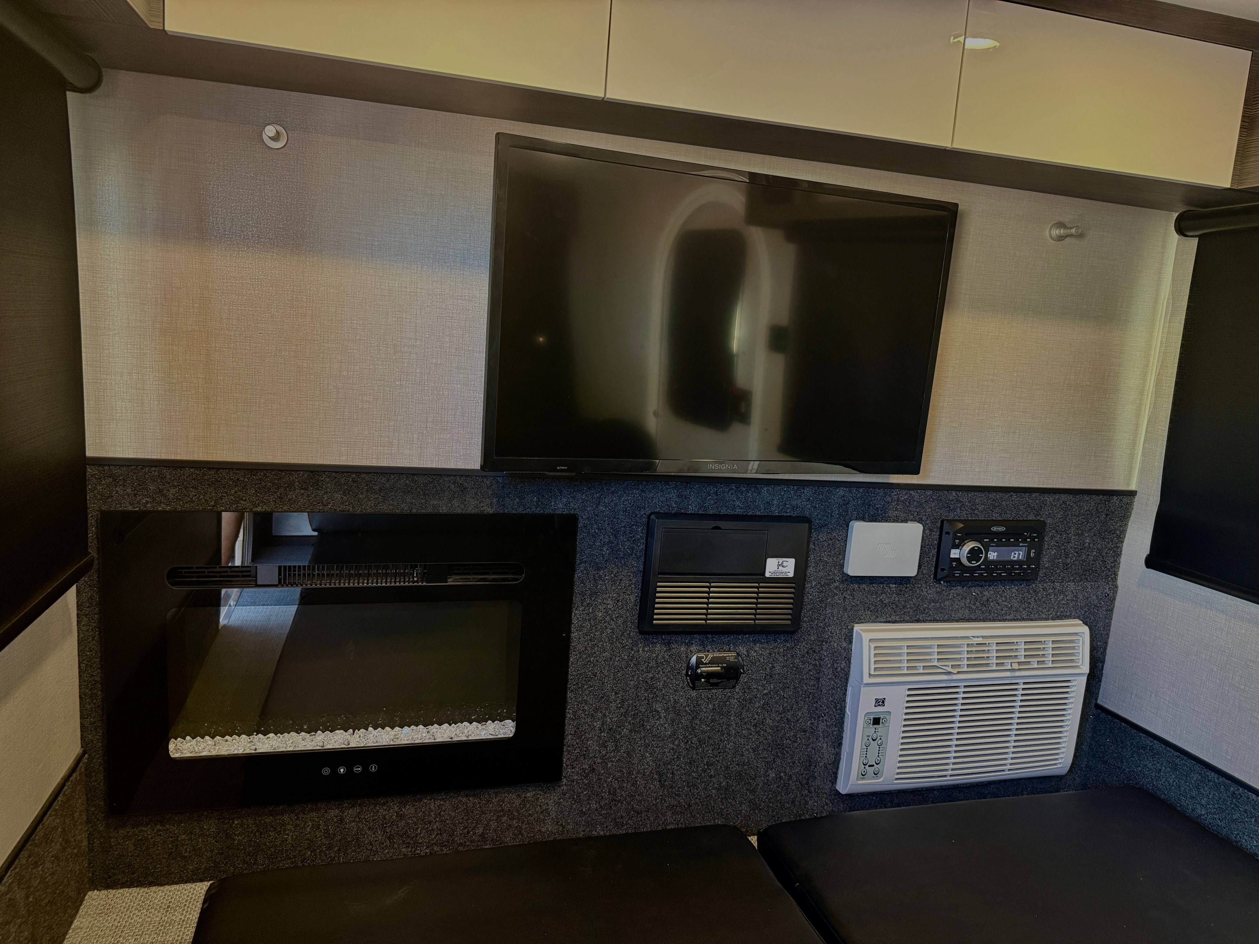 Inside an RV rental, a compact entertainment wall features a TV, electric fireplace, stereo, and AC unit above seating.. InTech RV Luna 2022