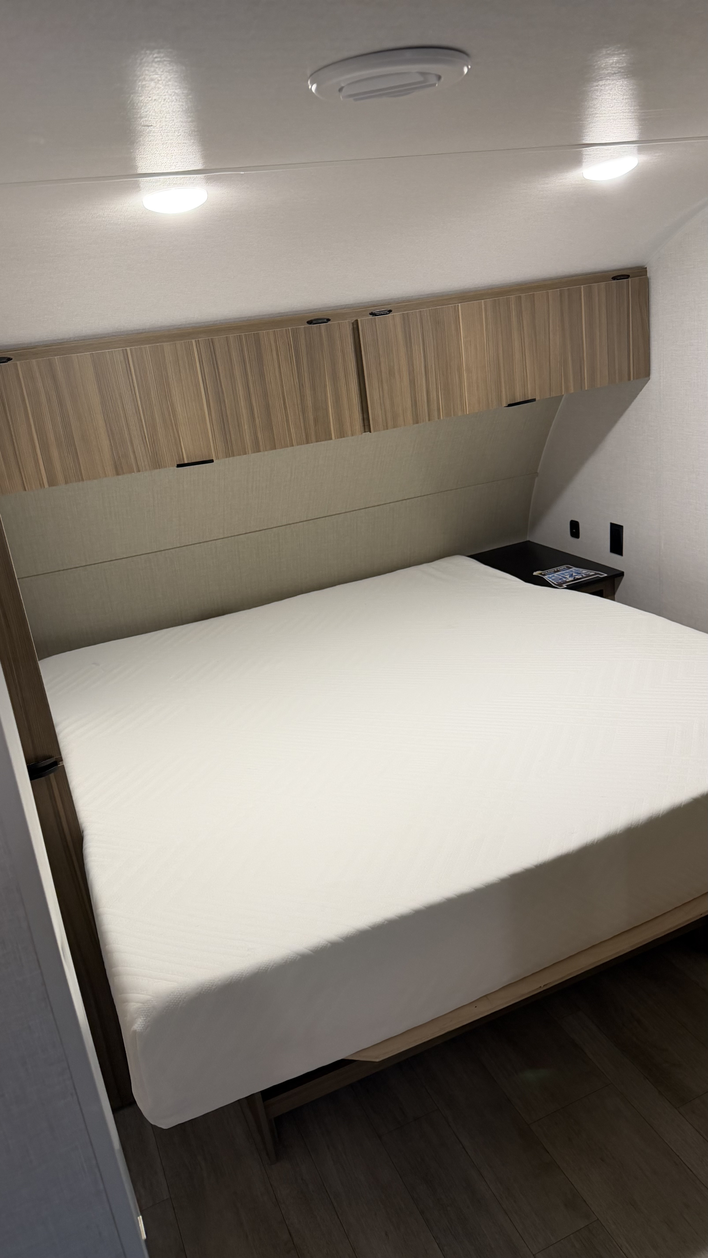 Inside an RV rental: a neat bedroom with a large bed, overhead wooden cabinets, and bright ceiling lights for a restful journey.. Forest River Salem Cruise-Lite 2025