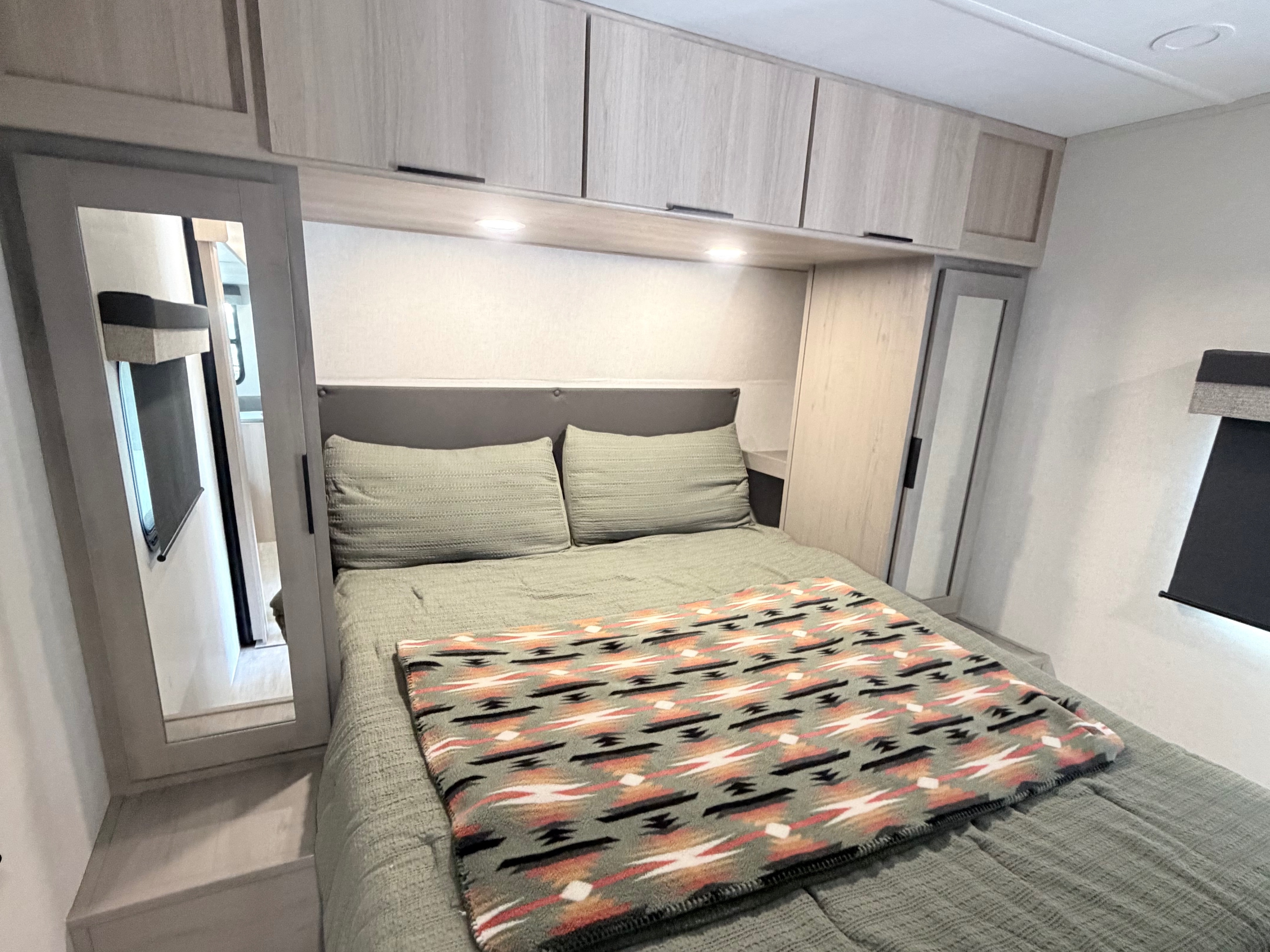 Cozy RV rental bedroom featuring a comfortable bed with a green comforter and Southwestern-patterned blanket, plus modern cabinets.. Dutchmen Kodiak 2026