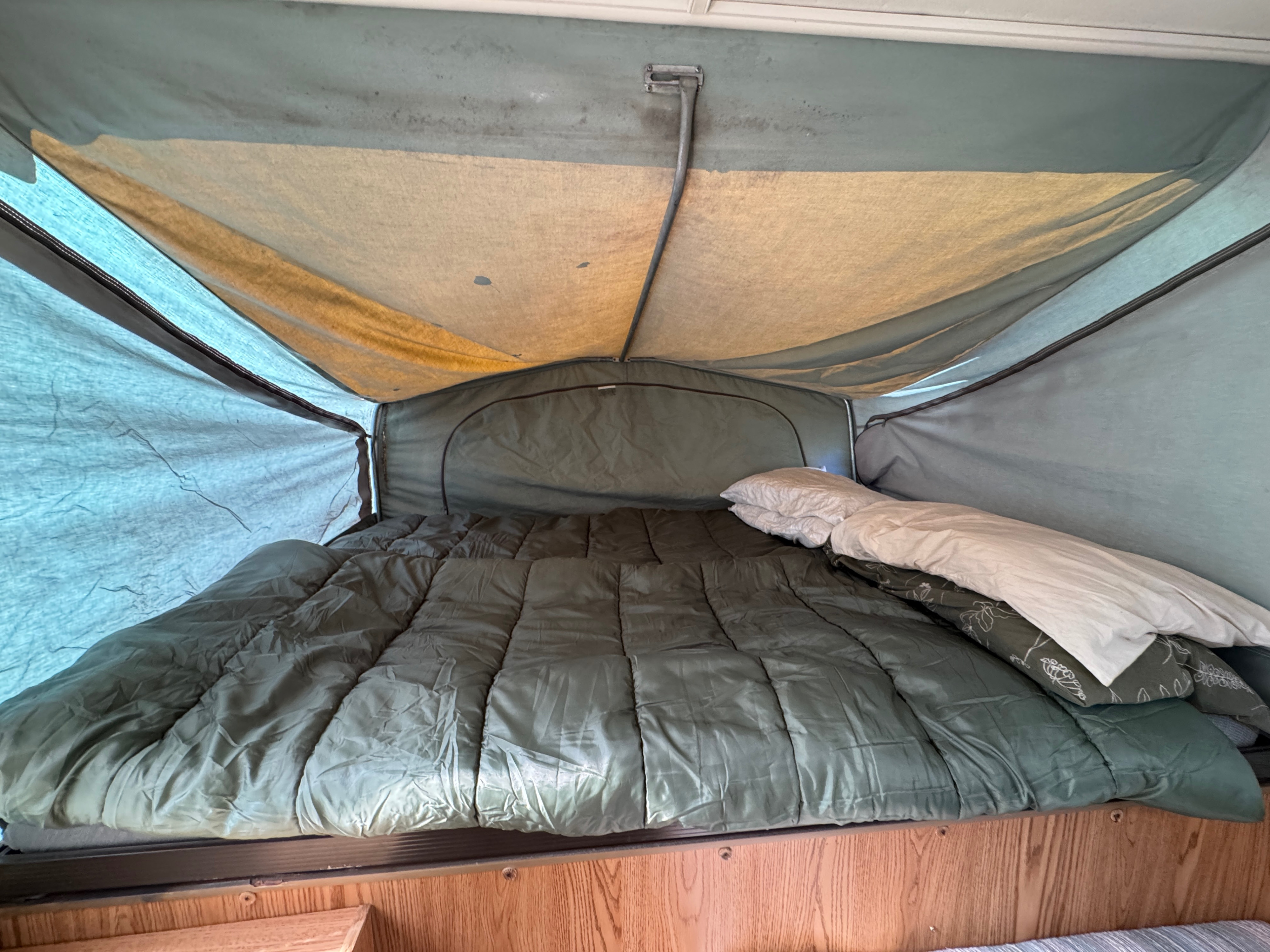 Inside an RV rental pop-up camper, a bed with a green comforter and white pillows, surrounded by fabric tent walls.. Jayco Jay Thrush 6 1989