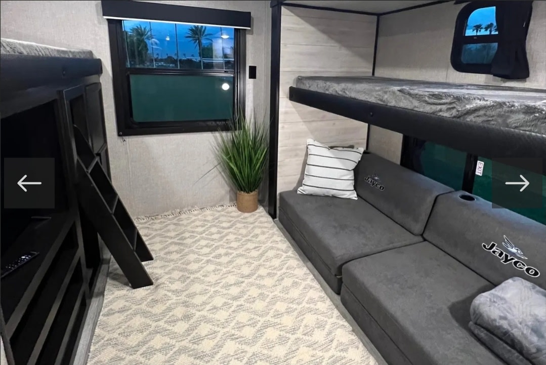 Modern RV rental: Bunk beds, gray Jayco sofa, potted plant, and patterned rug create a cozy interior scene.. Jayco Jay Flight 2022