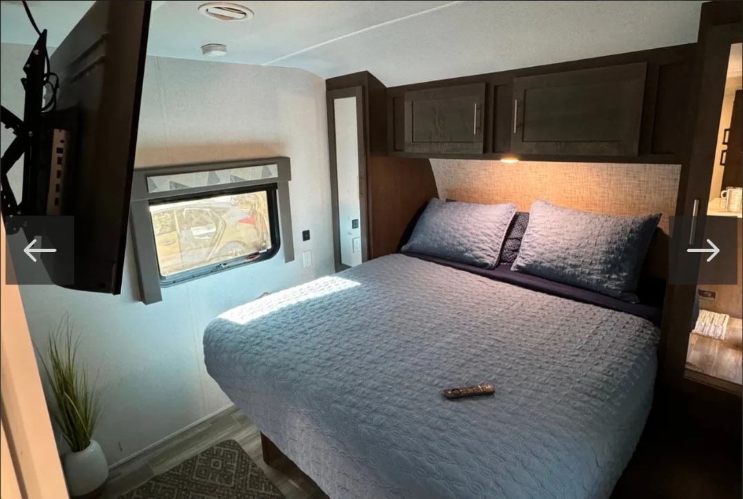 Cozy RV rental bedroom featuring a queen bed with blue bedding, mounted TV, window, and overhead storage for comfortable travel.. Forest River Other 2020