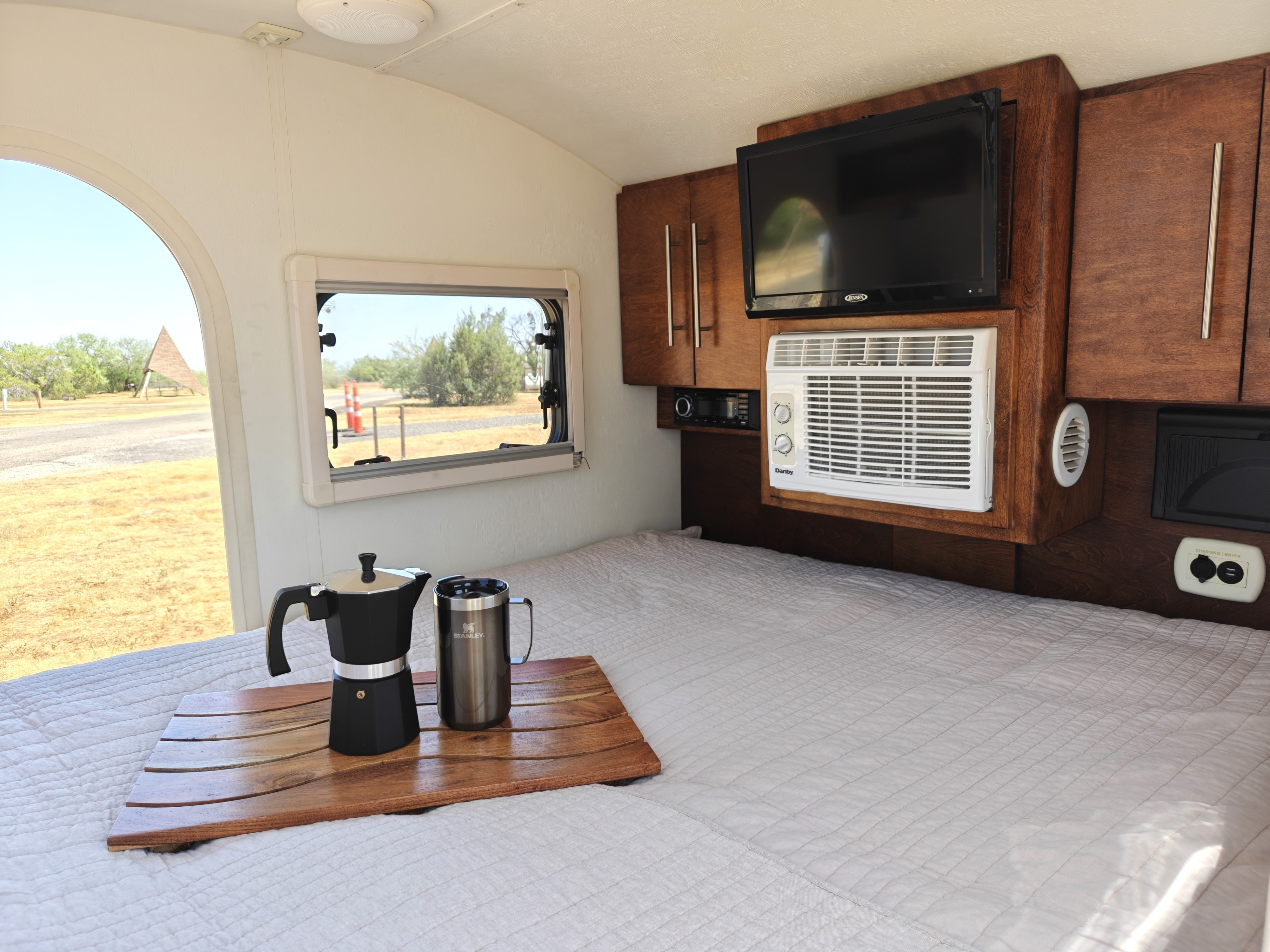 Compact RV rental interior: bed with coffee, TV, AC, charging, and outdoor views for comfortable travel.. nuCamp T@G 2018