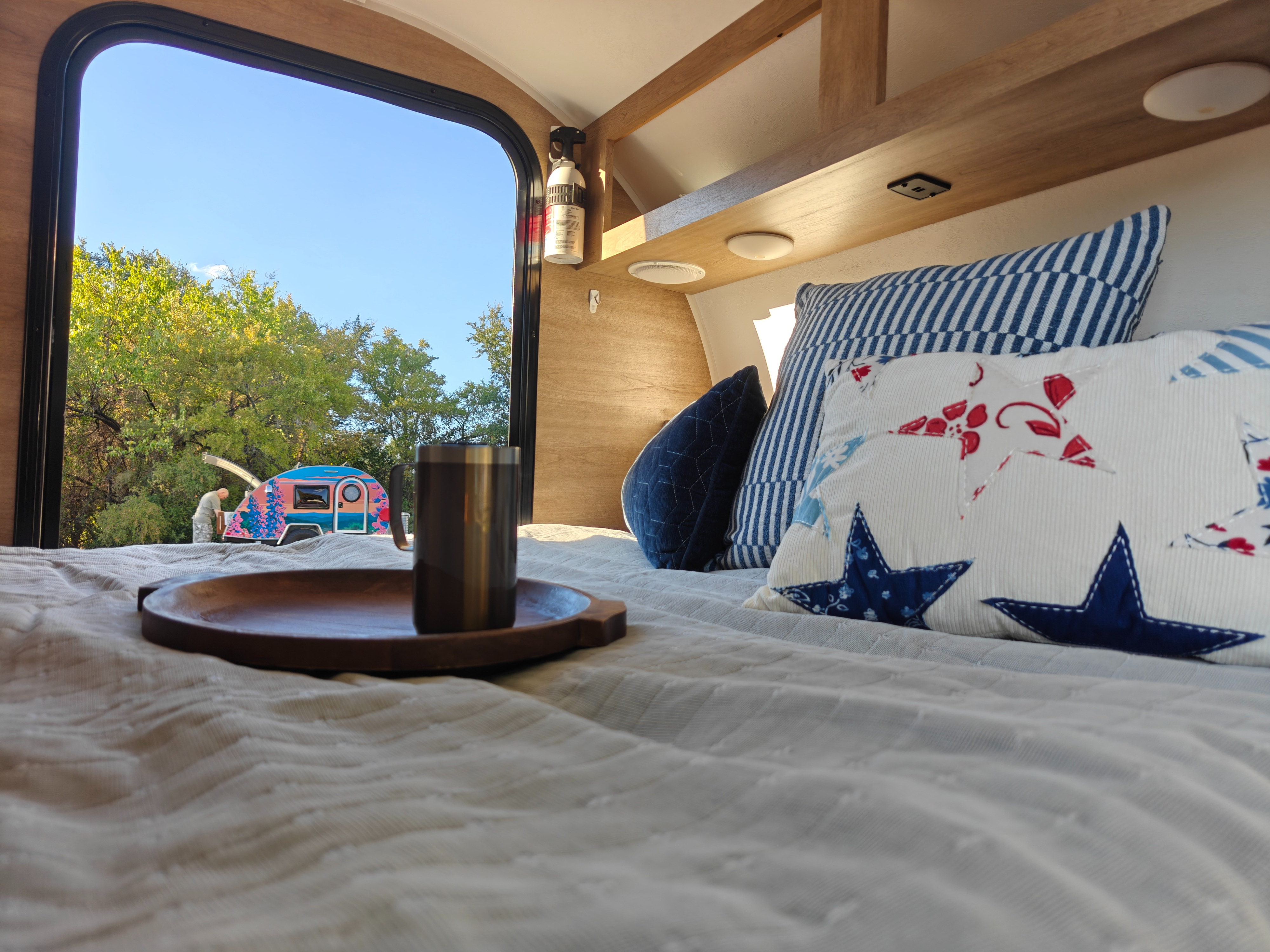 Start your adventure! Inside a cozy RV rental, a comfy bed offers views of nature & a colorful camper.. Braxton Creek Bushwhacker 2021