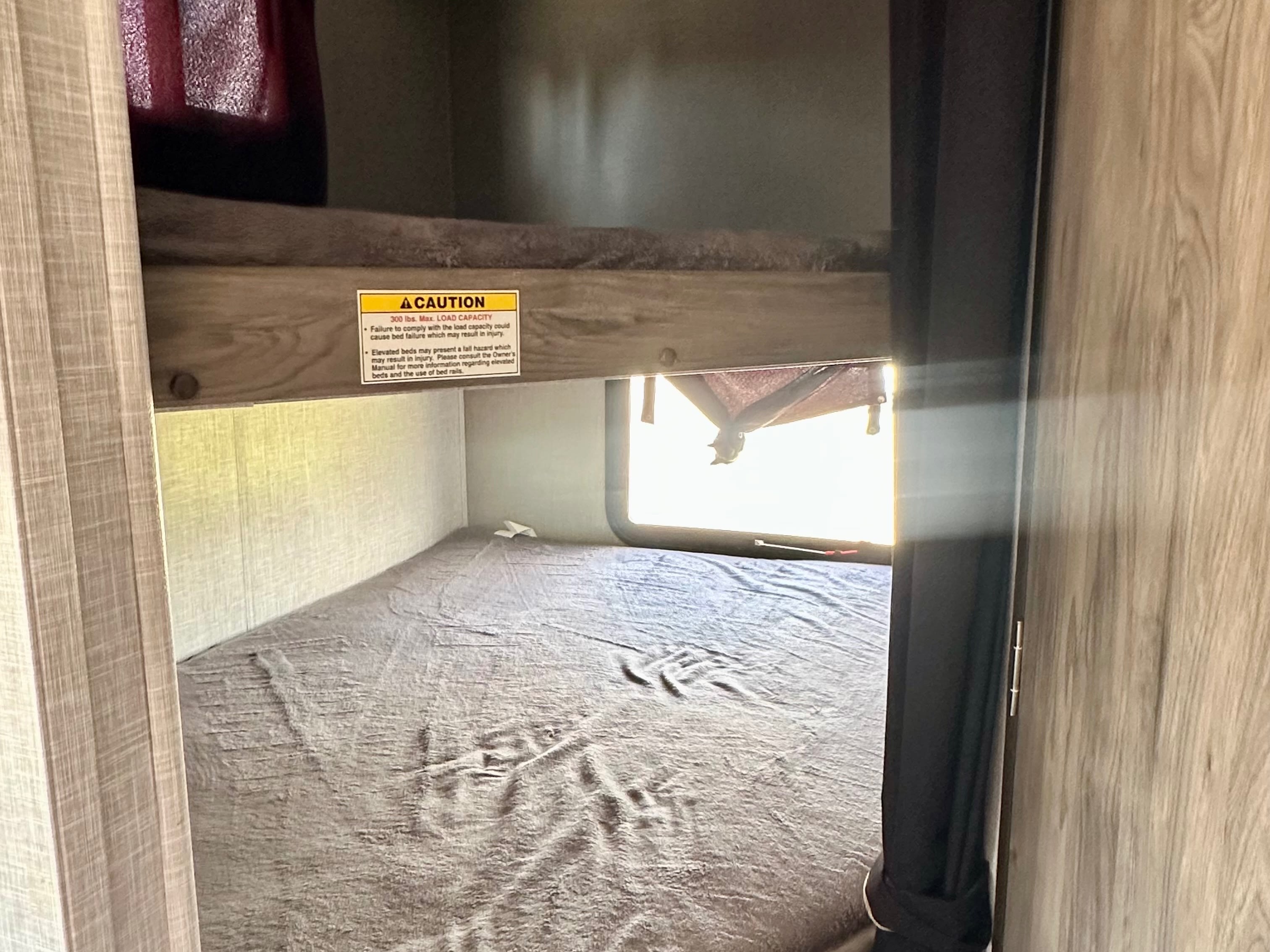 RV rental bunk beds: upper bunk has a 300lb max load caution. Lower bunk visible, bright window, and privacy curtains.. Crossroads RV Zinger Lite 2021