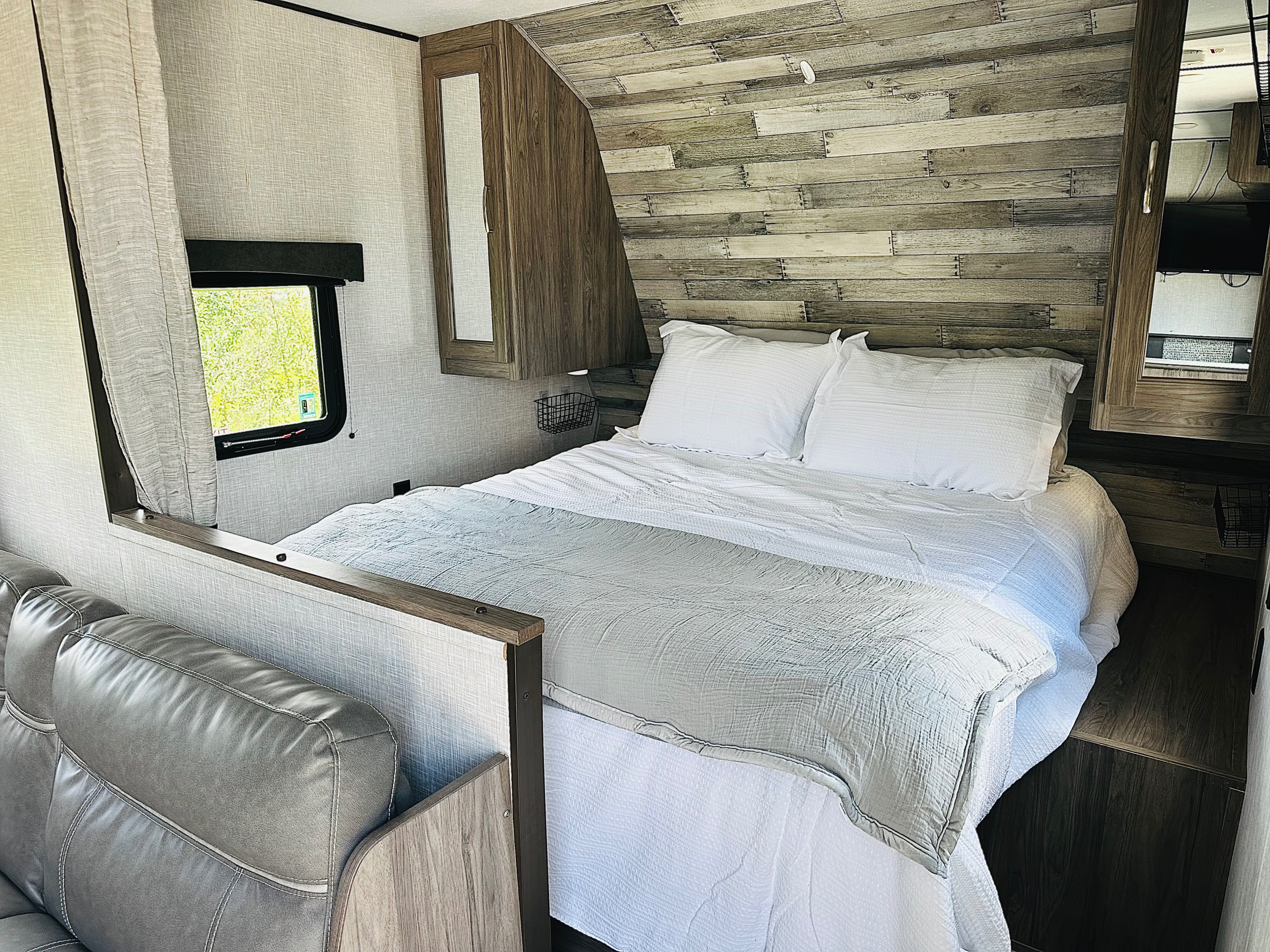 Enjoy comfort in this RV rental bedroom: cozy bed, rustic wood wall, window views, and integrated sofa for relaxing travels.. Crossroads RV Zinger Lite 2021