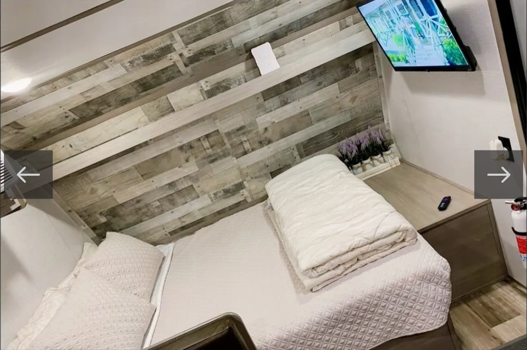 Cozy RV rental bedroom featuring a bed, wood accent wall, wall-mounted TV, bedside table with lavender, and safety extinguisher.. Dutchmen Coleman Lantern LT 2022